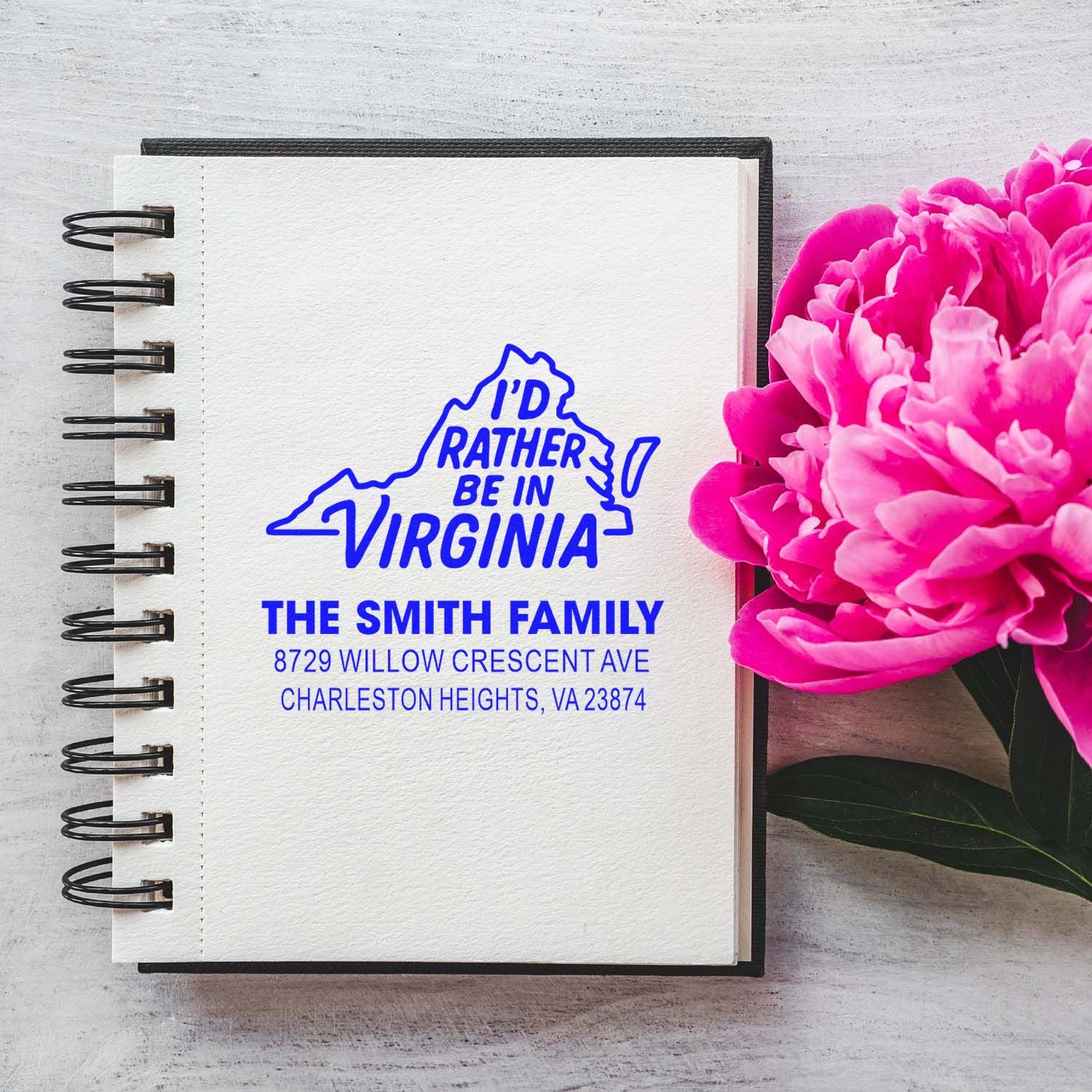 Custom Virginia address stamp on a spiral notebook beside pink peonies, featuring Id Rather Be in Virginia and The Smith Family address.