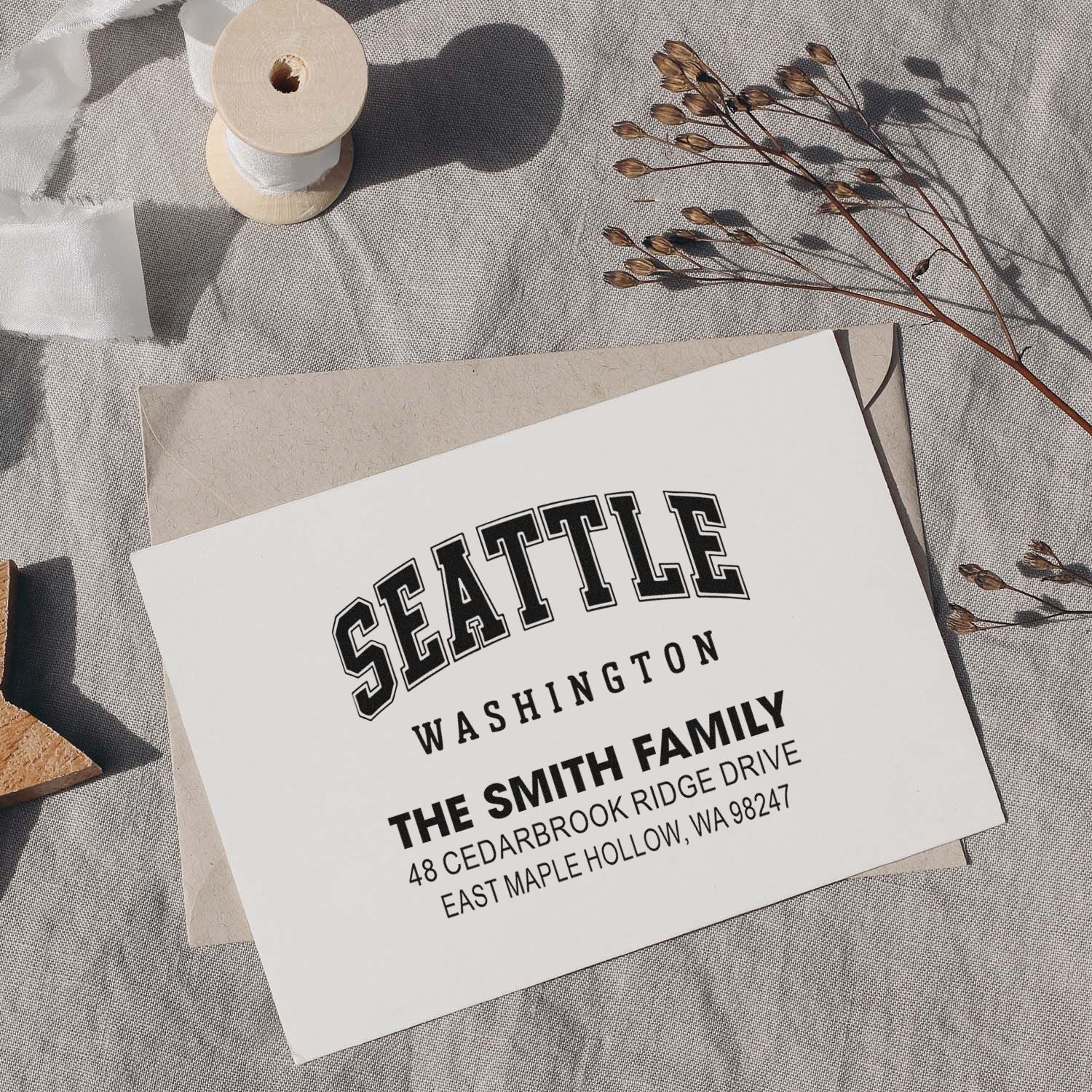 Custom Seattle Washington family return address stamp on envelope, styled with ribbon spool and dried florals on a linen tabletop.