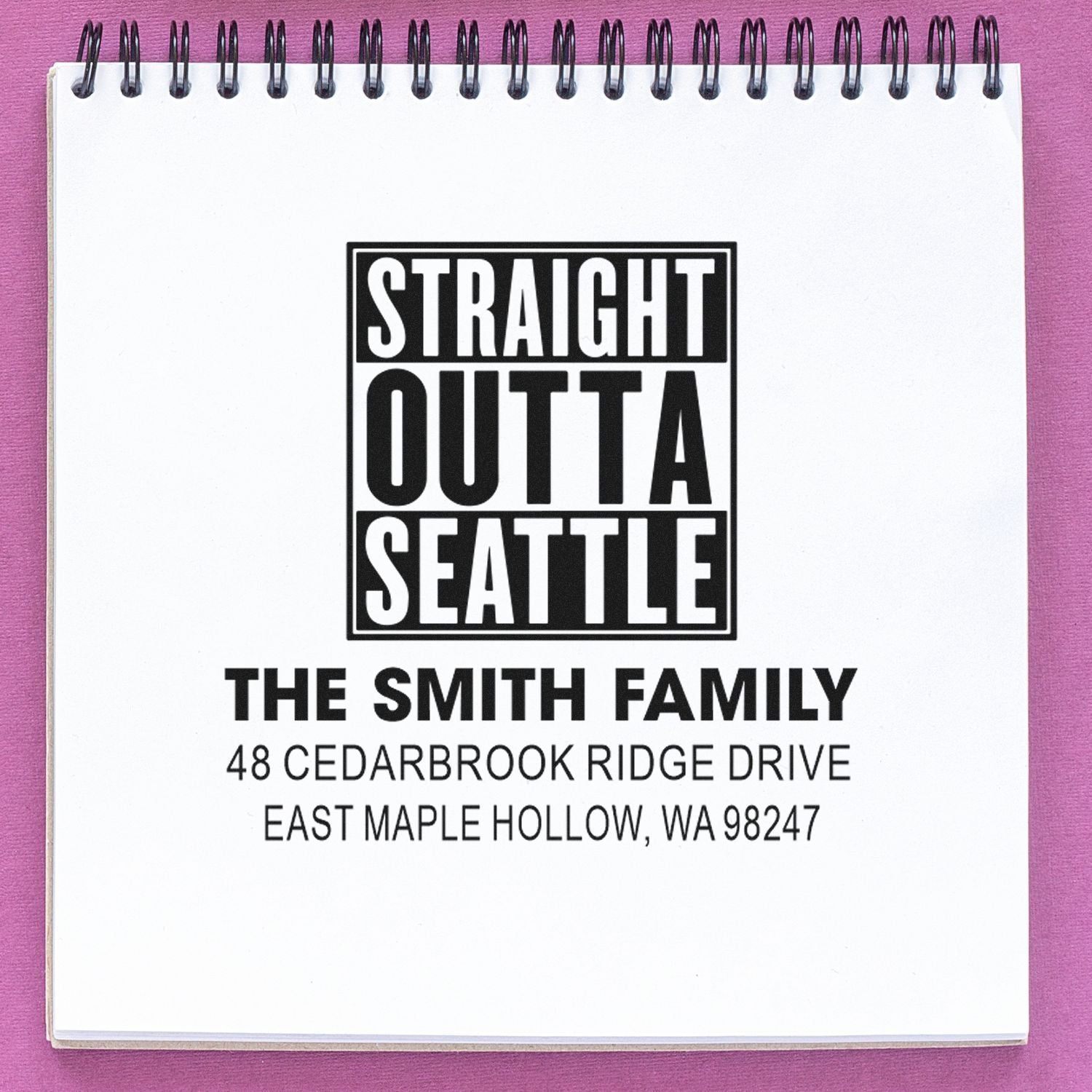 Custom self-inking return address stamp with Straight Outta Seattle design, The Smith Family name, and Seattle-area address on a spiral notebook.