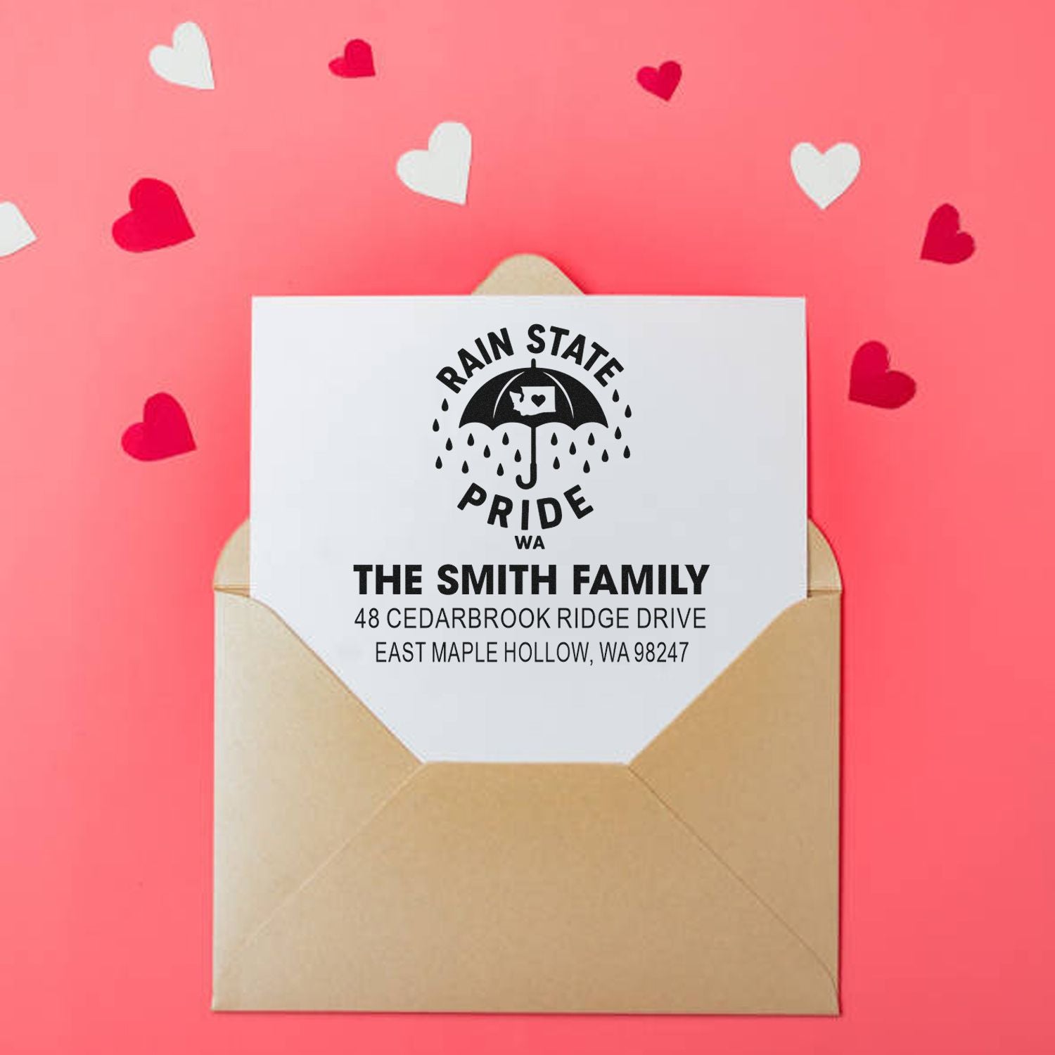 Custom return address stamp on a white card in a kraft envelope, with pink hearts on a coral background and Rain State Pride WA family address.