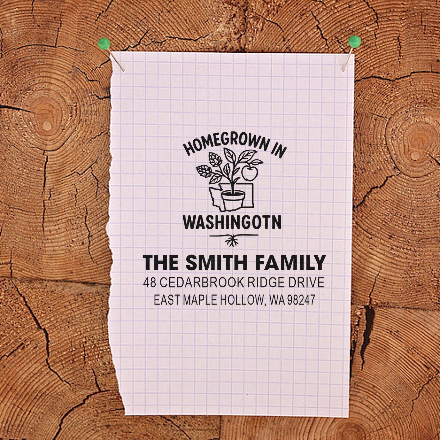 Personalized return address stamp for The Smith Family, with Homegrown in Washington plant design, pinned to graph paper on a wood log background.