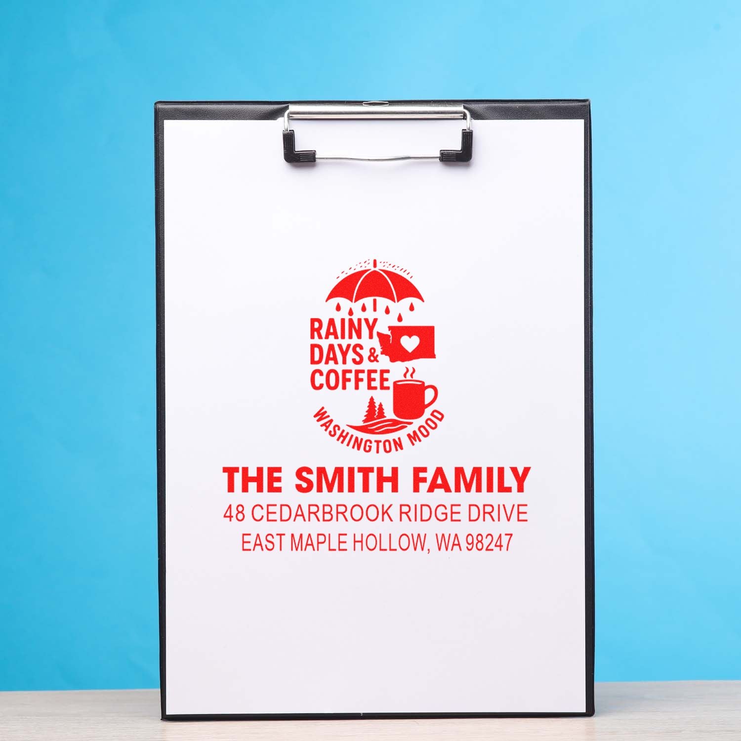 Custom address stamp on clipboard with red Rainy Days & Coffee Washington Mood design and The Smith Family address on blue background.