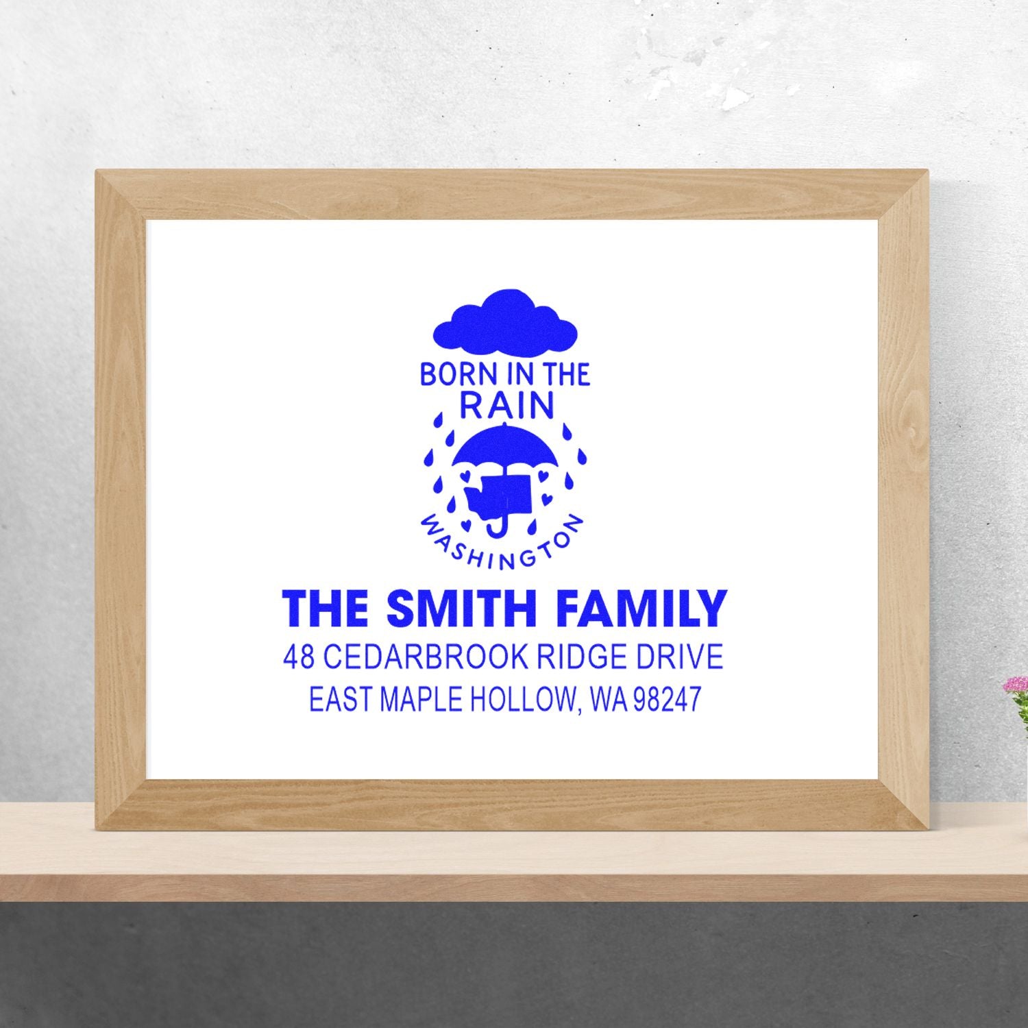 Framed custom address stamp featuring blue Born in the Rain Washington design for The Smith Family, displayed on a shelf.