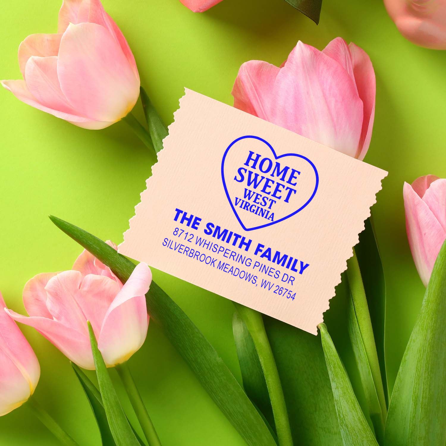 Custom address stamp with blue Home Sweet West Virginia heart design on beige paper, surrounded by pink tulips on a bright green background.