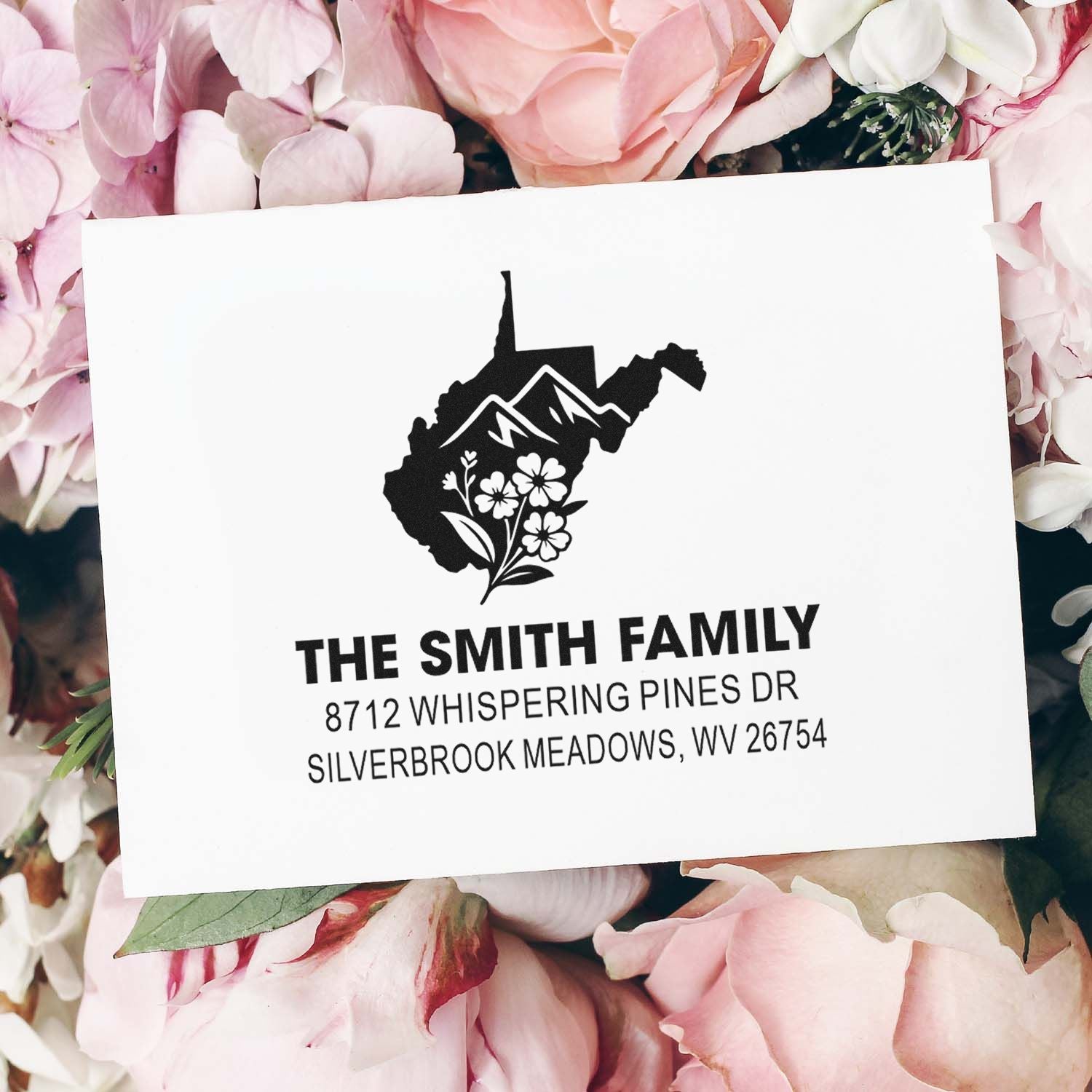 Custom family address stamp with West Virginia mountain and floral design on a white card, surrounded by pink flowers.