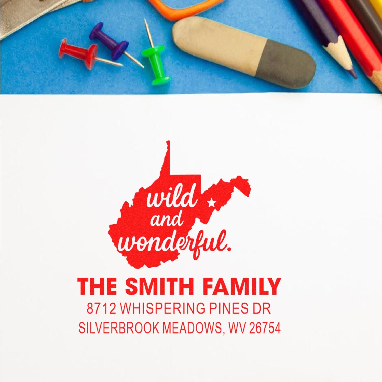 Custom address stamp featuring West Virginia outline and wild and wonderful text, displayed with colorful push pins, pencils, and eraser on blue desk.