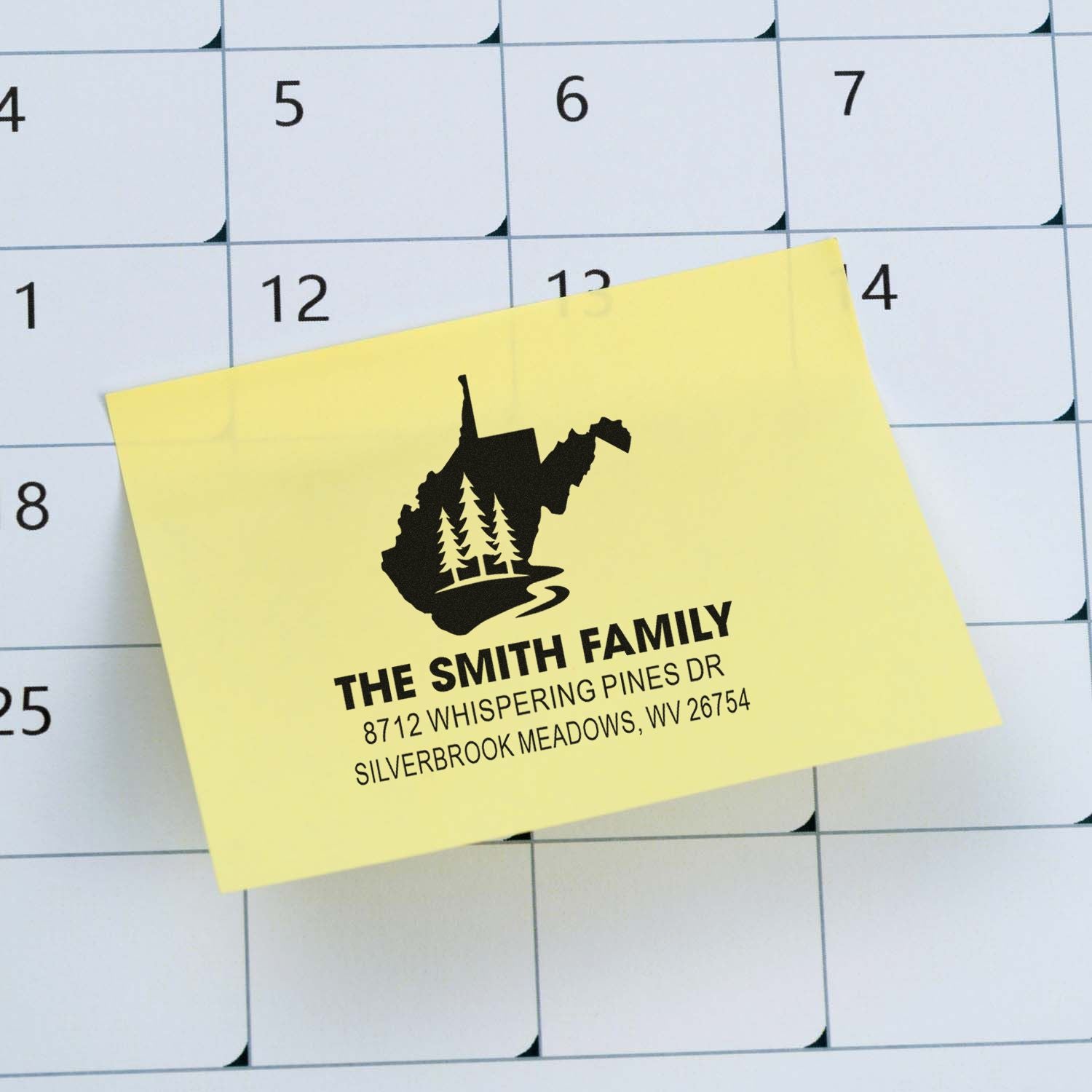 Personalized family address stamp on a yellow sticky note over a monthly calendar, with West Virginia silhouette, pine trees, and home address.