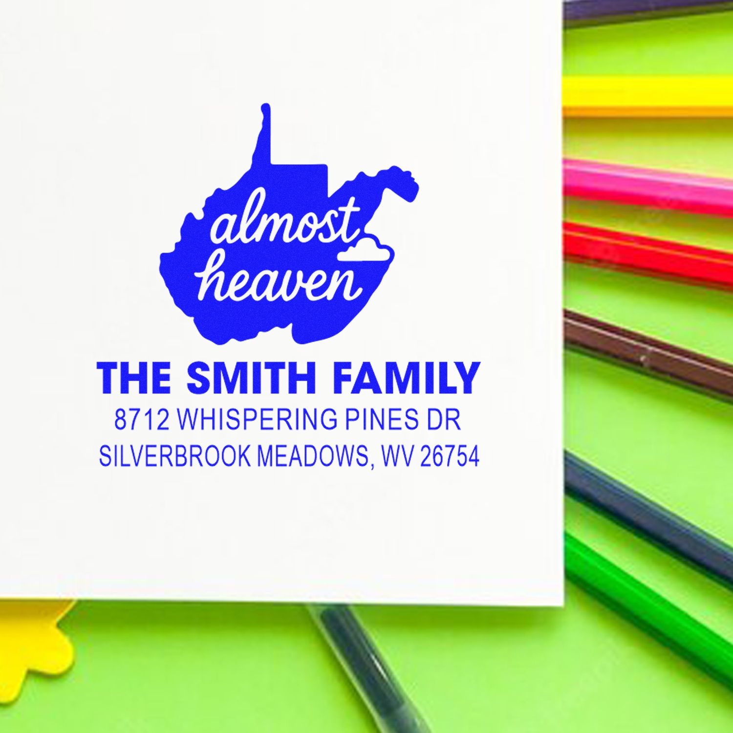 Personalized West Virginia address stamp with almost heaven design for The Smith Family, shown beside colorful ink pads.