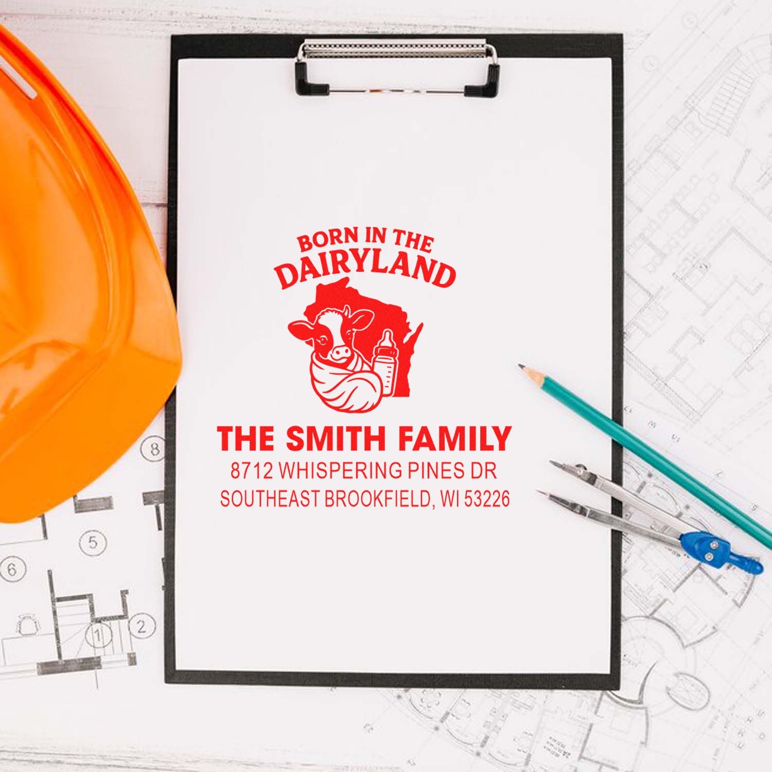 Custom self-inking dairy-themed family stamp with cow and bottle, displayed on a clipboard with hard hat, pencils, and blueprints.