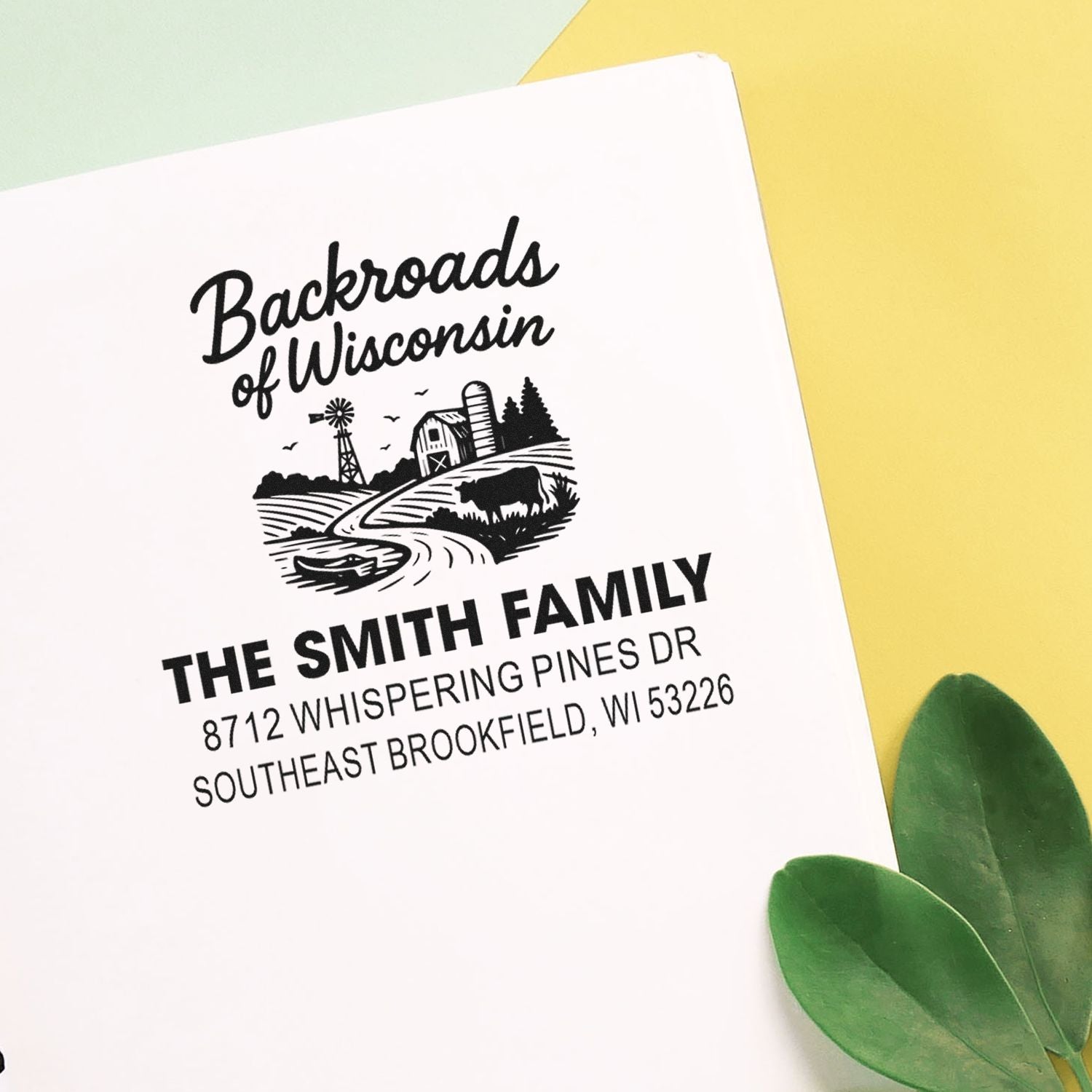 Custom Backroads of Wisconsin family address stamp on white paper, featuring a farm scene, on a pastel yellow background with green leaves.