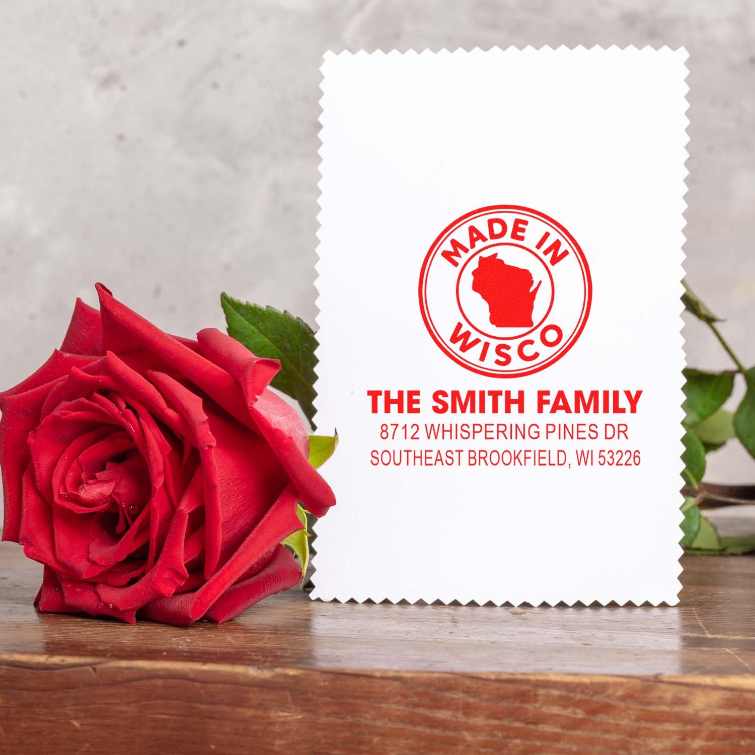 Custom Made in Wisconsin family address stamp with logo, displayed beside a red rose on a wooden table.
