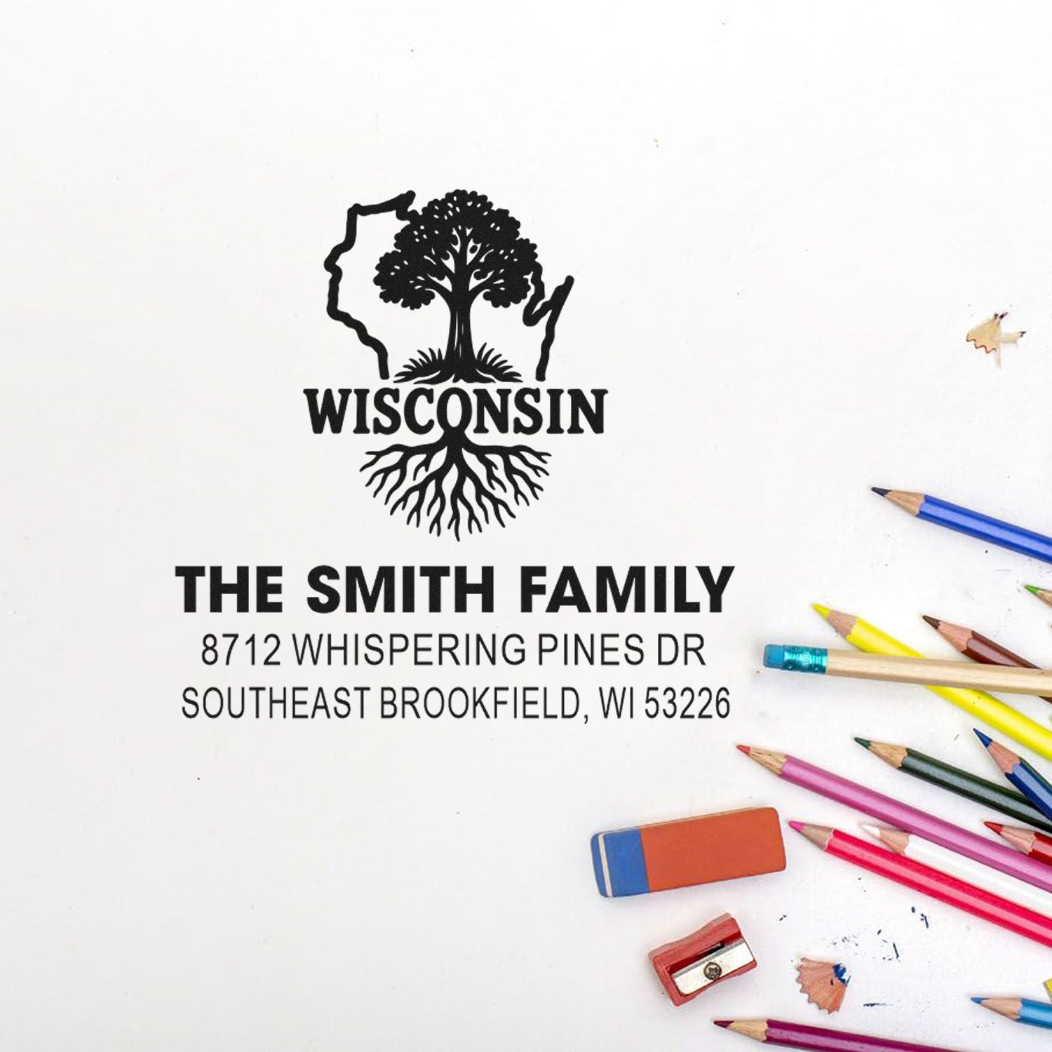 Custom Wisconsin address stamp for The Smith Family, with state tree logo, on white background beside colored pencils, eraser and sharpener.