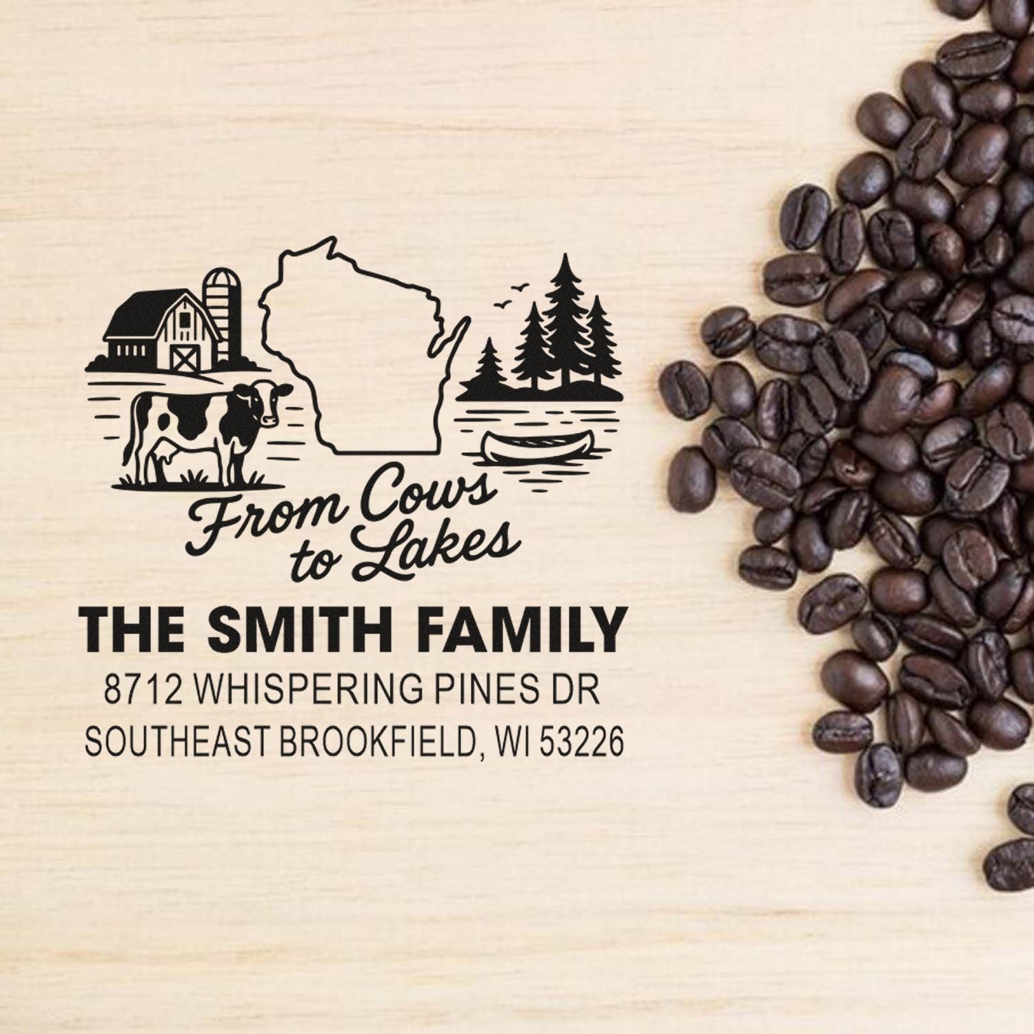 Custom Wisconsin family address stamp with barn, cow, lake and pine trees on wood background beside coffee beans.