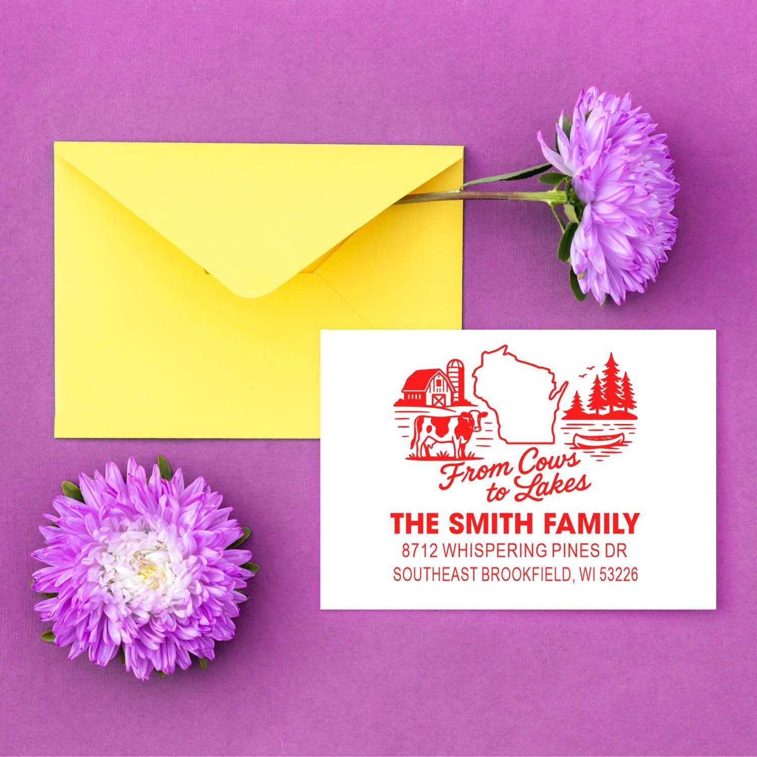 Custom red Wisconsin address stamp with farm and lake design beside a yellow envelope and purple flowers on a purple background.