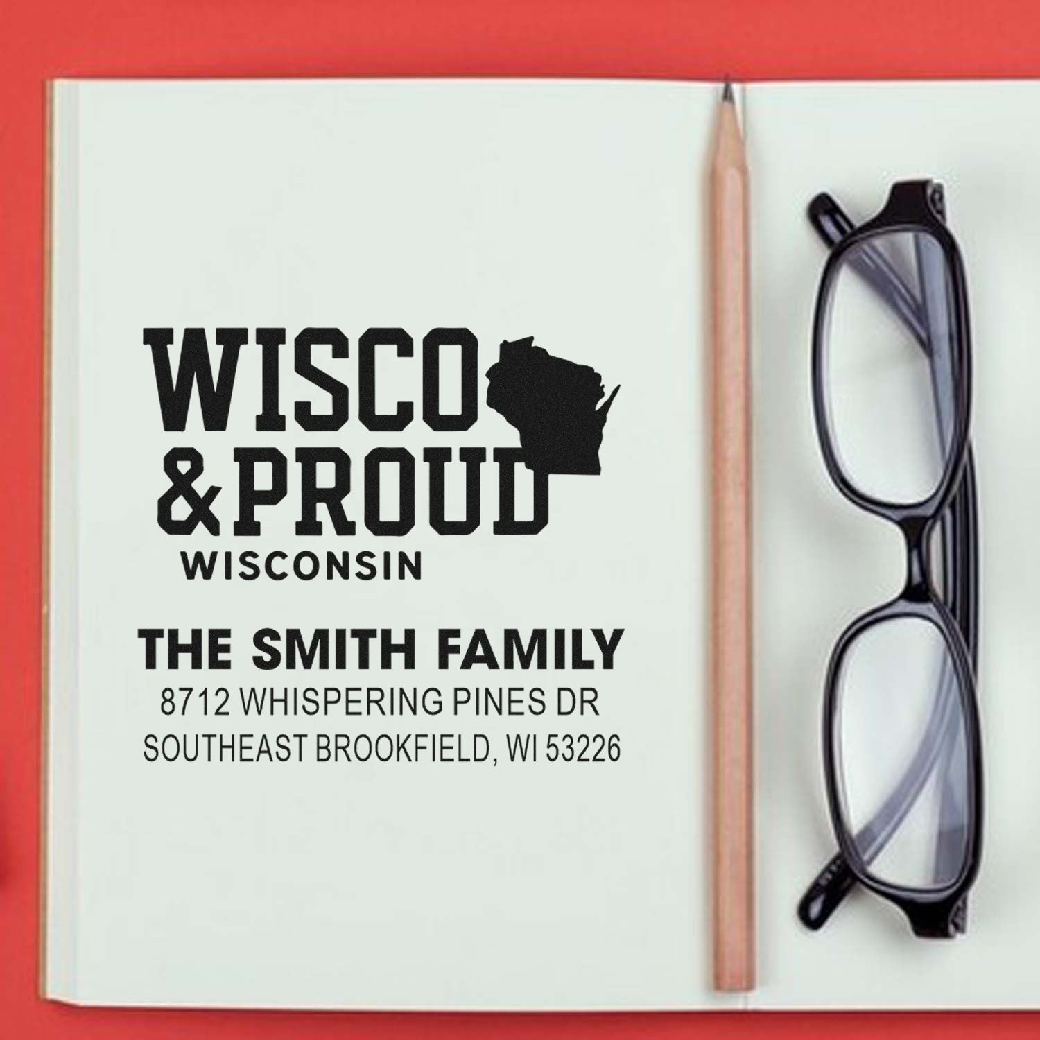 Wisconsin & Proud custom address stamp on open notebook with pencil and eyeglasses, personalized for The Smith Family in Southeast Brookfield, WI.