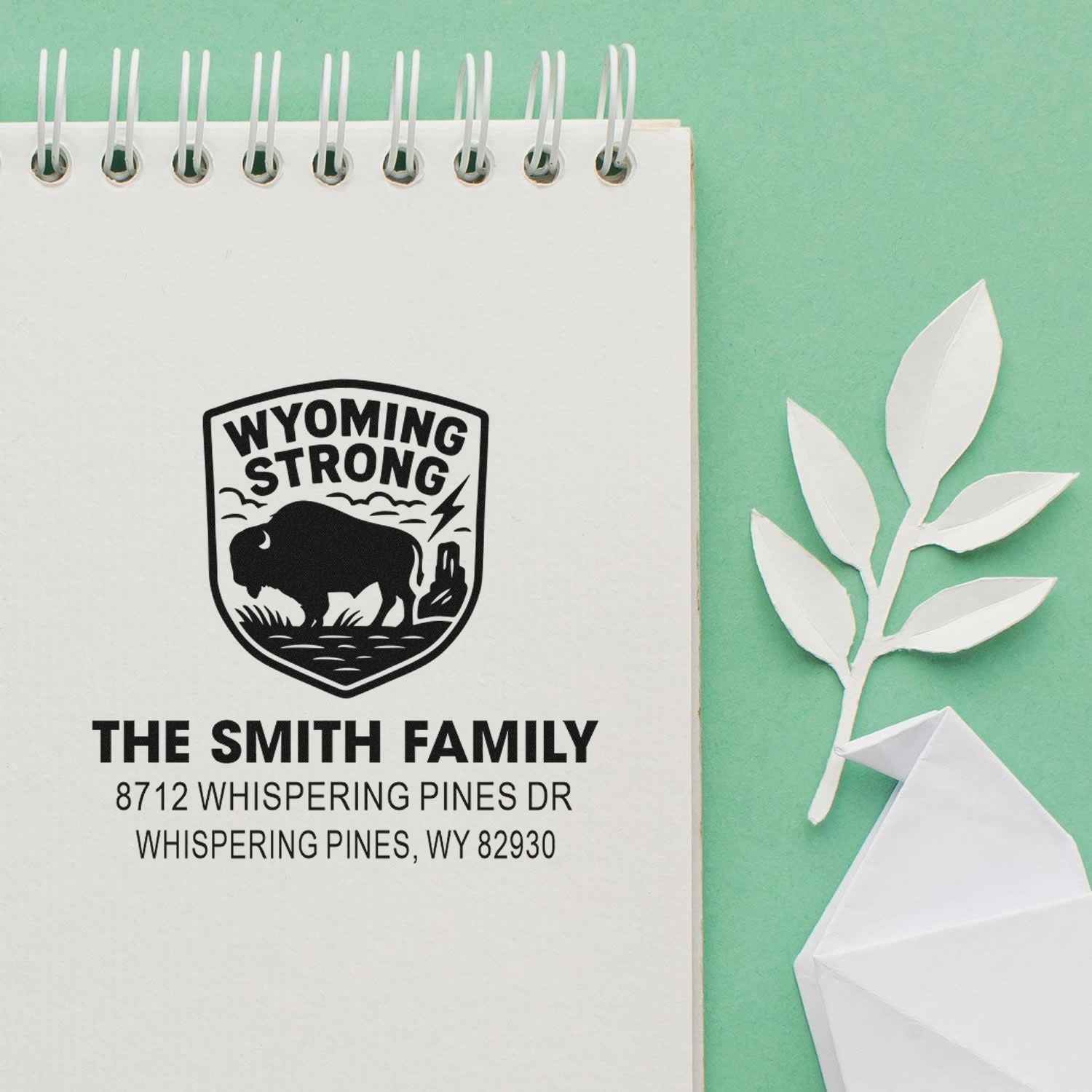 Custom Wyoming Strong return address stamp for The Smith Family on a notepad, featuring a bison emblem, address, paper leaf, and origami bird on mint background.