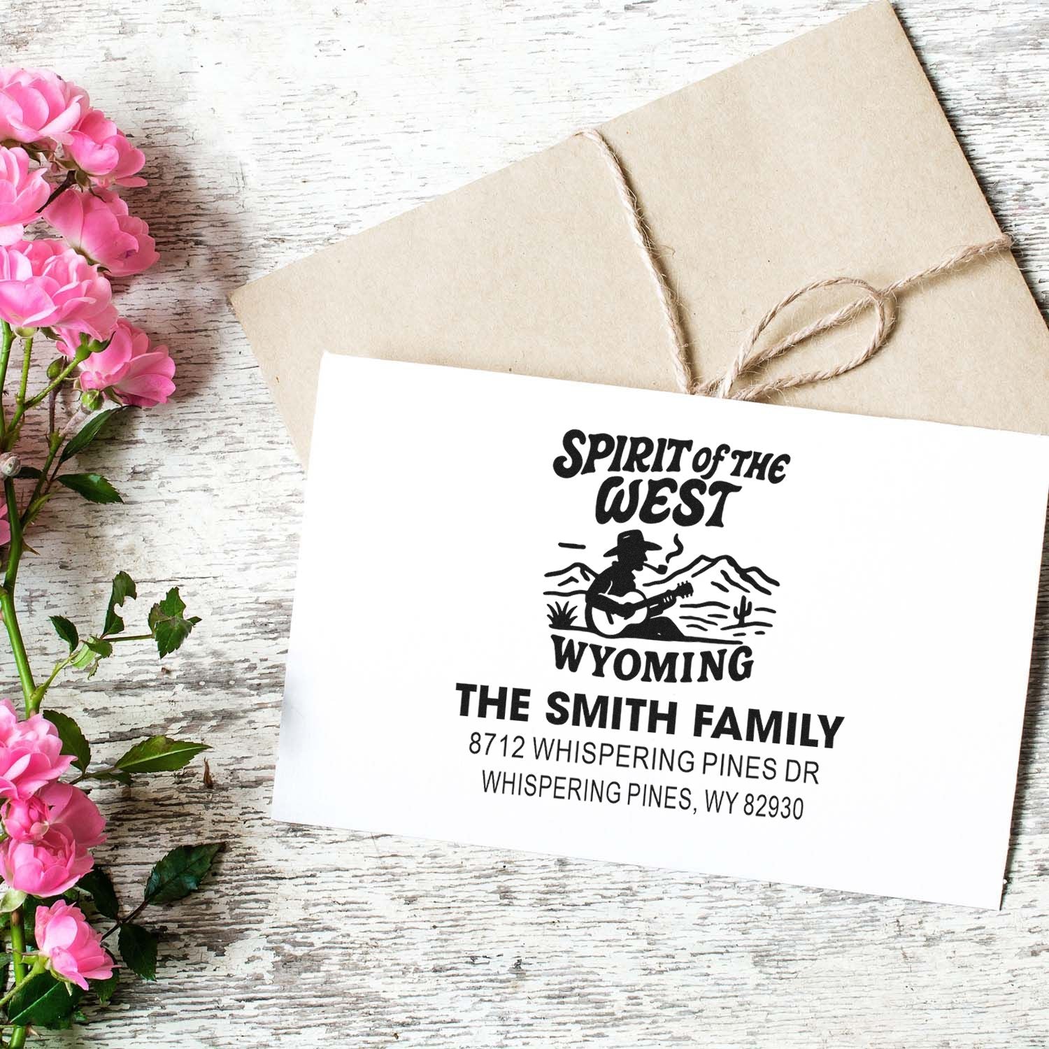 Custom Spirit of the West Wyoming return address stamp on envelope, featuring a cowboy guitar design on rustic twine-wrapped mail with pink flowers.
