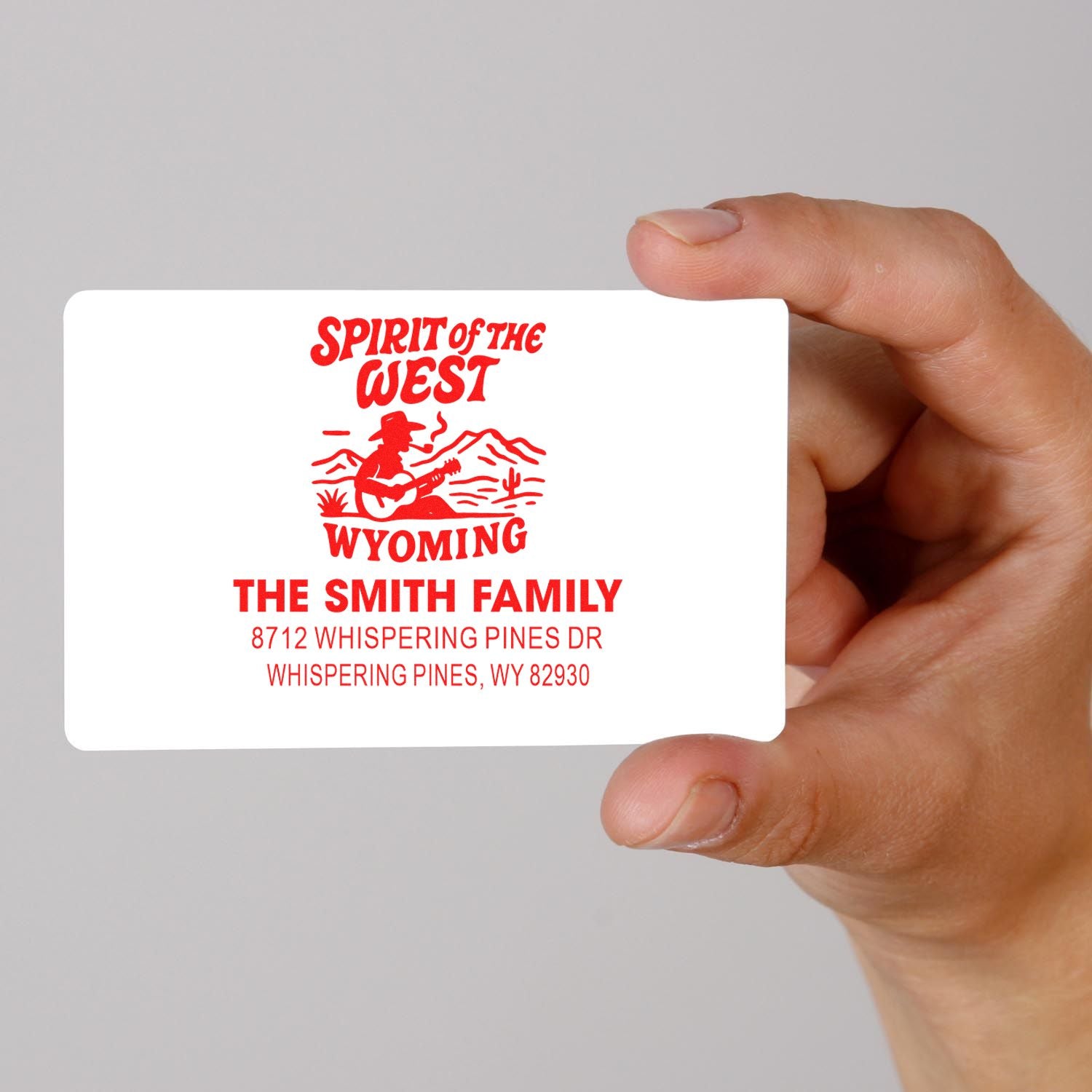 Hand holding custom red return address stamp with Spirit of the West Wyoming cowboy design, Smith Family address on white background.