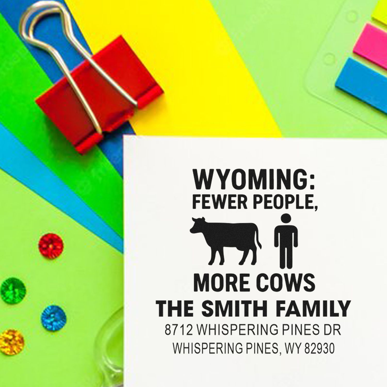 Custom Wyoming address stamp reading Fewer People, More Cows for The Smith Family, on colorful stationery with paperclips and sticky notes.