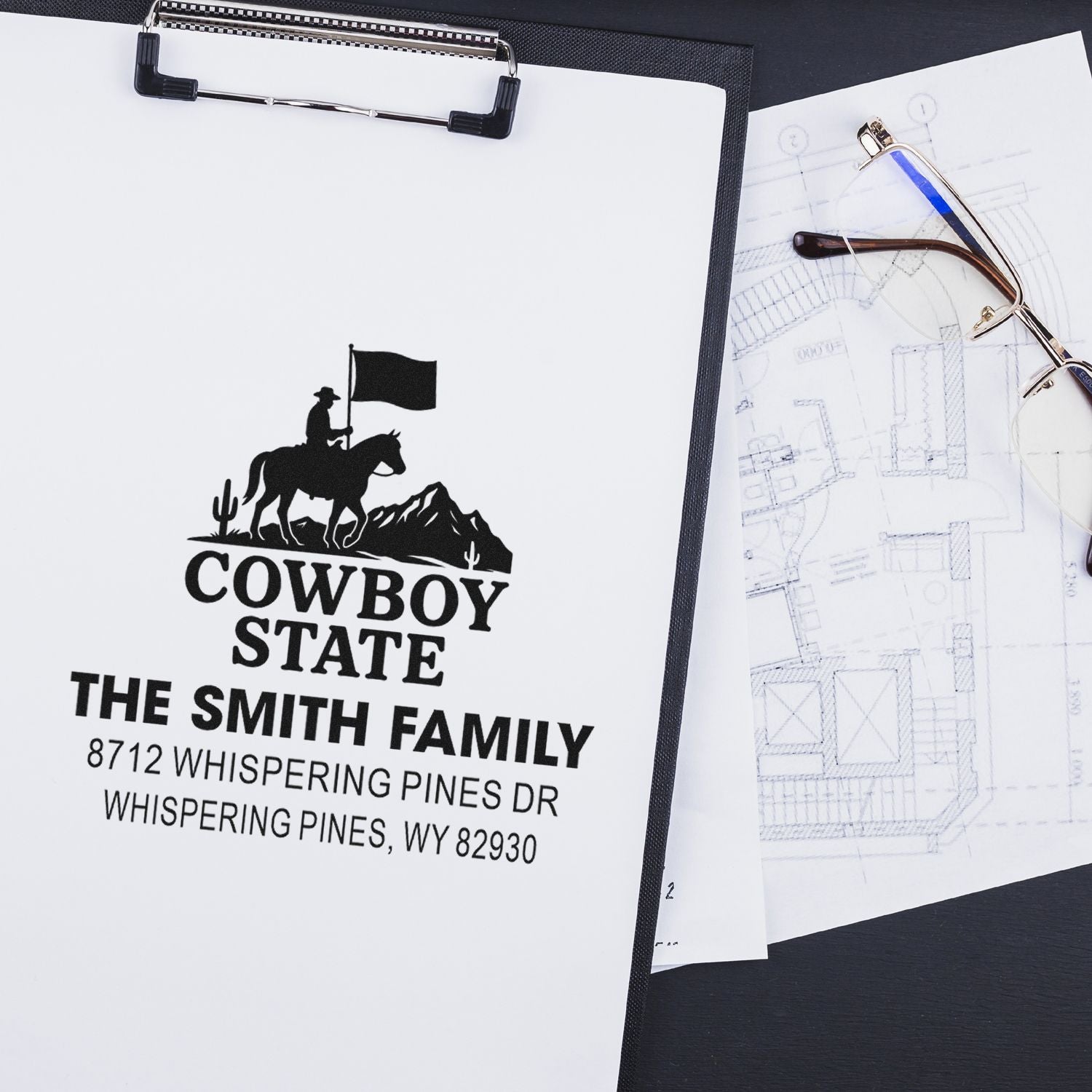 Custom cowboy return address stamp with rider silhouette, family name, and Wyoming address on clipped proof sheets beside eyeglasses.