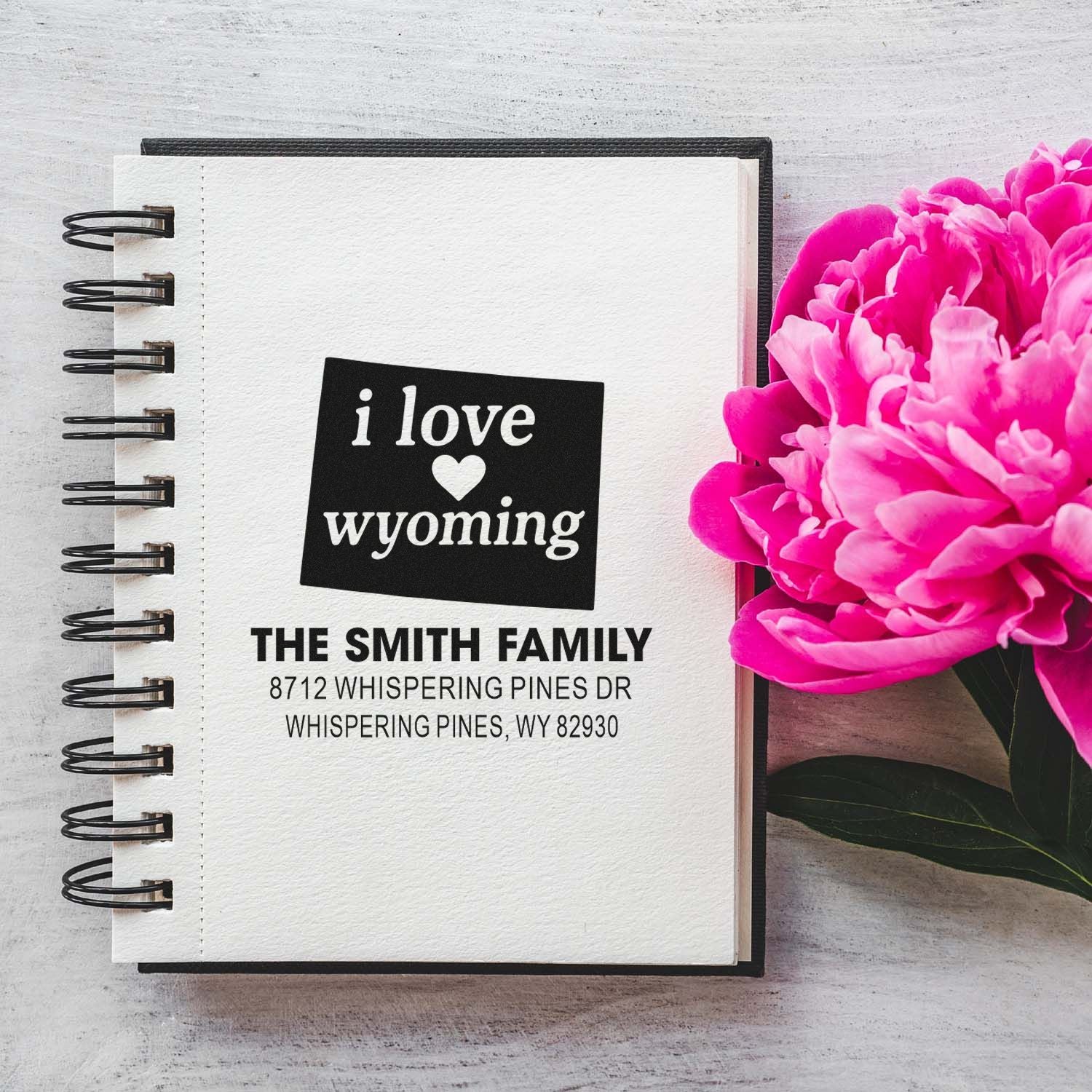 Personalized Wyoming return address stamp on a spiral notebook beside pink peonies, featuring i love wyoming and The Smith Family address.