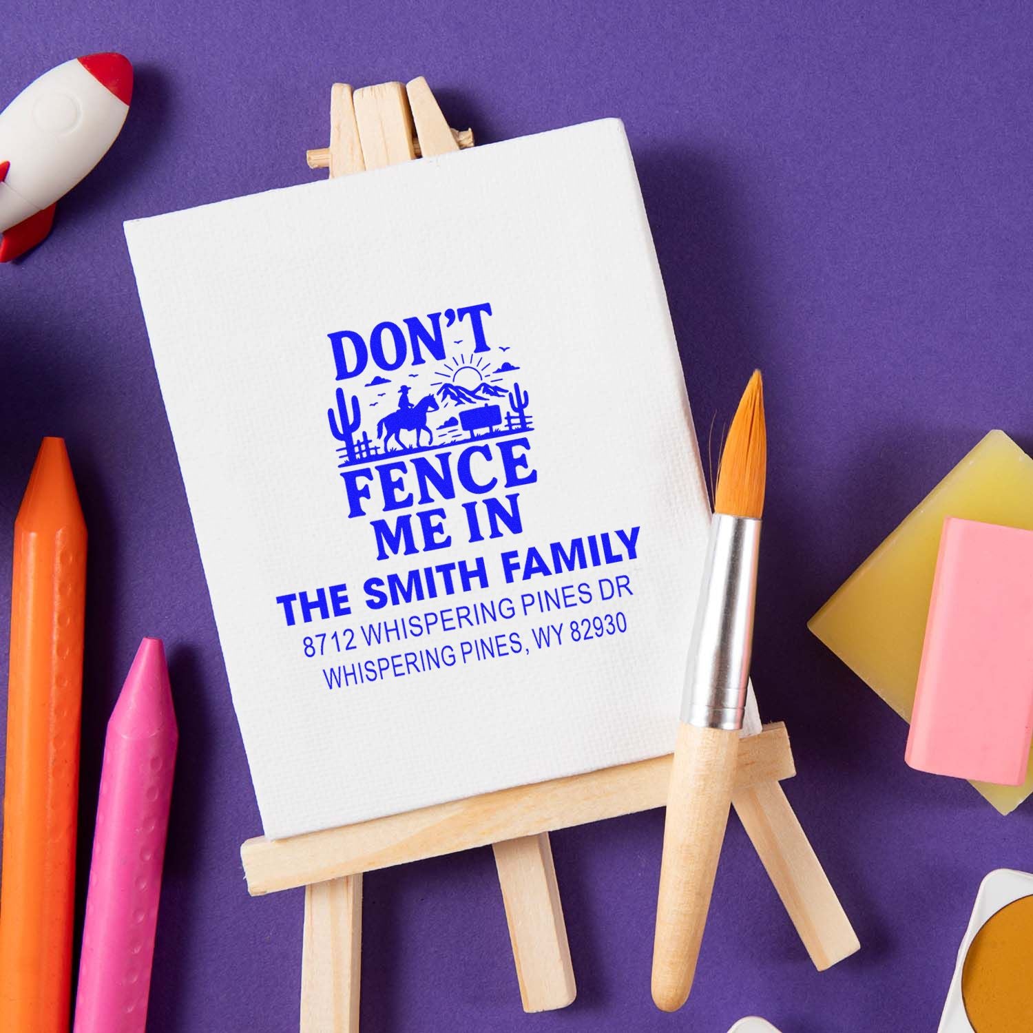 Custom Dont Fence Me In address stamp displayed on a mini easel with paintbrush and colorful stationery on a purple background.