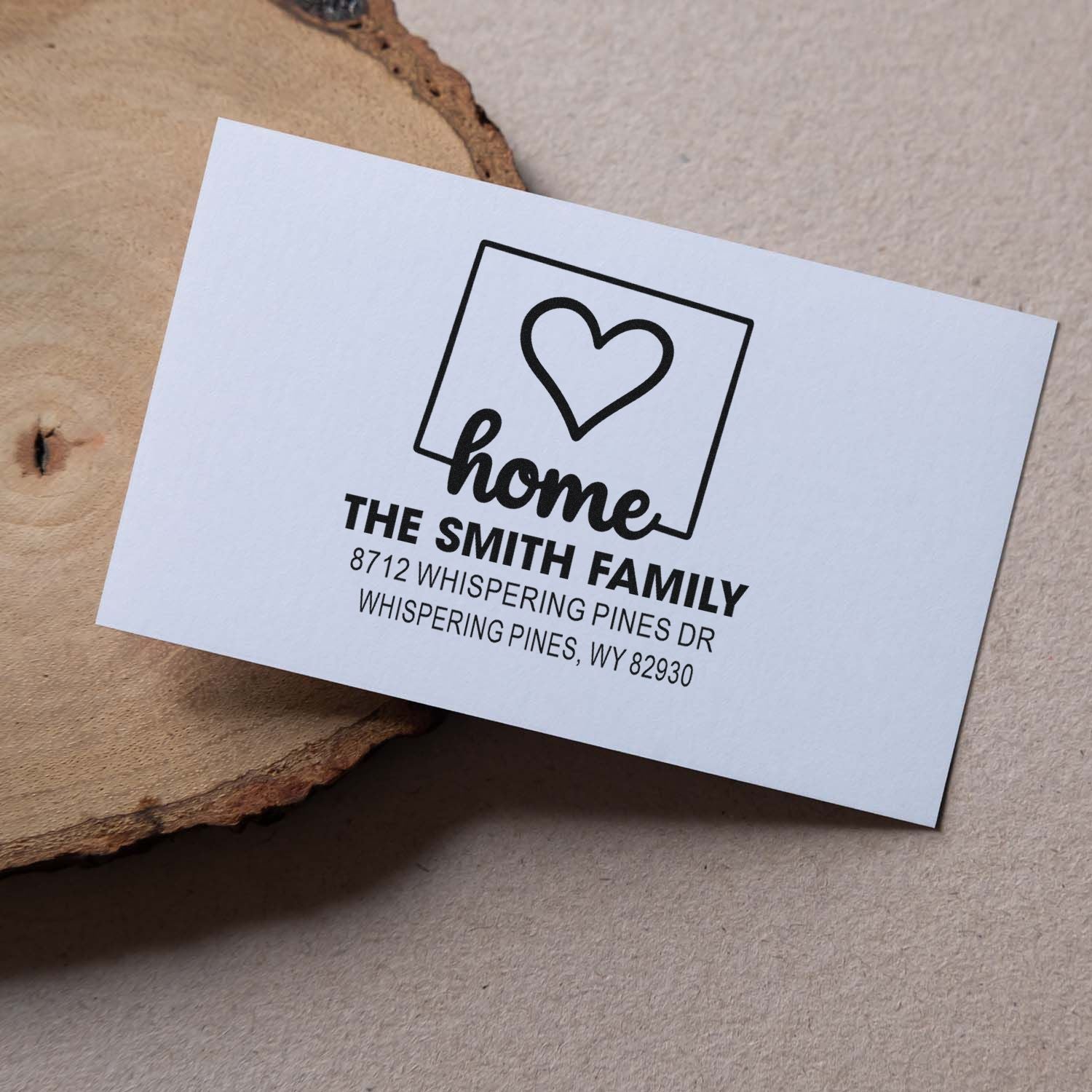 Custom home address stamp with heart icon and The Smith Family on a white card, styled on rustic wood for personalized mailing.