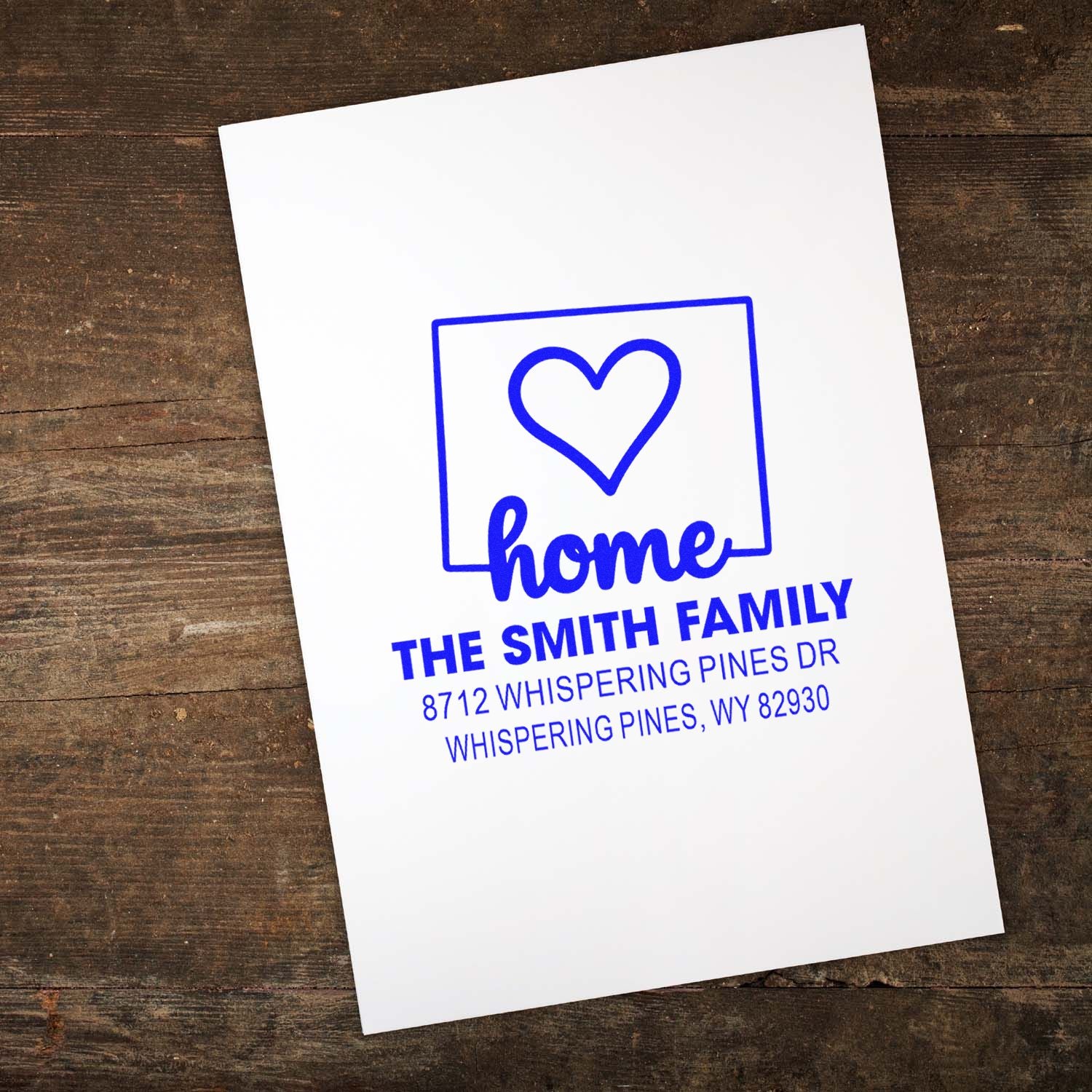 Custom blue return address stamp with heart and home design for The Smith Family, printed on white paper over a rustic wood background.
