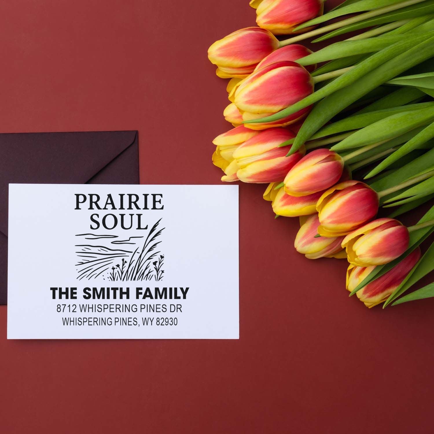 Custom Prairie Soul family address stamp beside yellow-pink tulips and a burgundy envelope on a maroon backdrop.