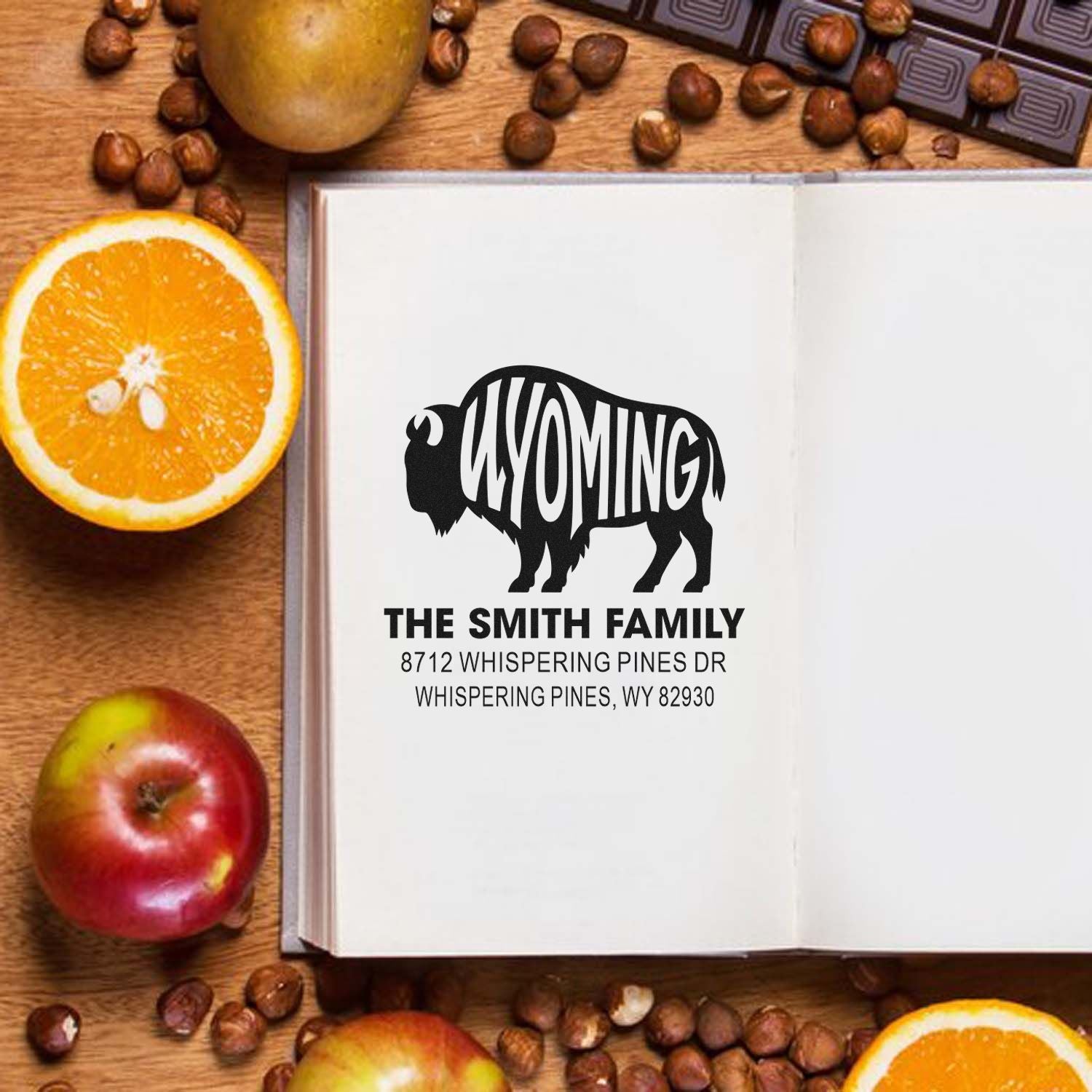 Open notebook featuring a custom Wyoming bison family address stamp for The Smith Family, styled on a wooden table with oranges, apples, and coffee beans.