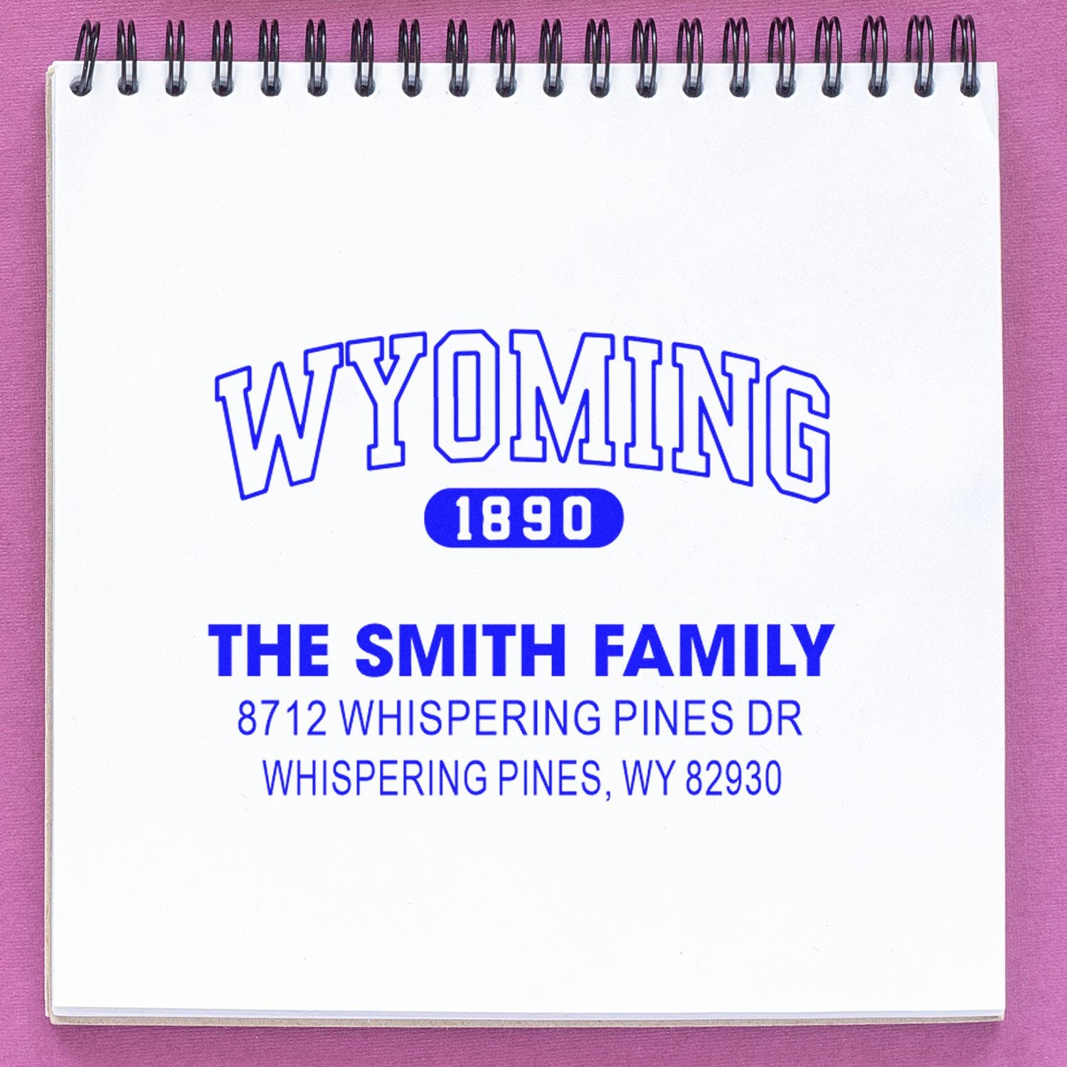 Custom Wyoming 1890 family address stamp in blue ink on a spiral notebook page, reading The Smith Family, Whispering Pines, WY.
