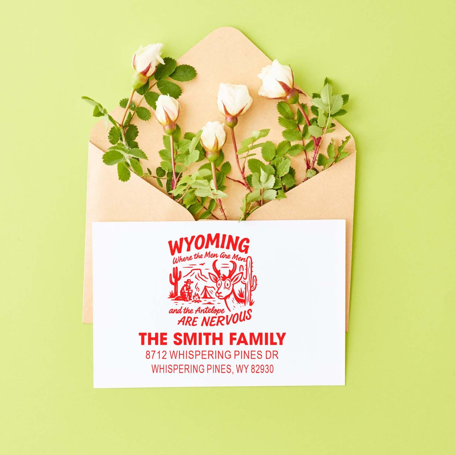 Custom Wyoming family address stamp on a white card in a tan envelope, accented with white rosebuds on a lime green background.