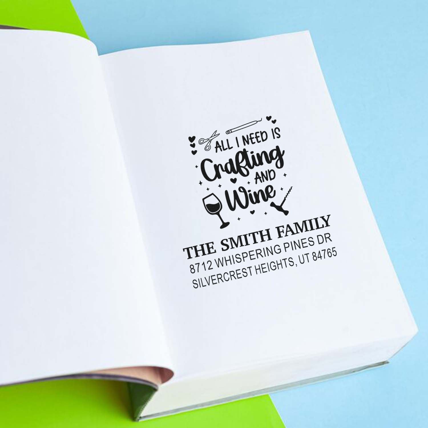 Custom return address stamp on open white paper with All I Need Is Crafting and Wine design, scissors, wine glass, and family address on blue background.
