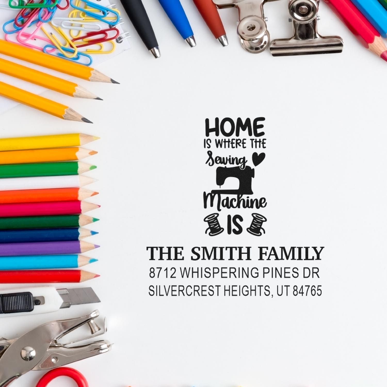 Custom sewing home address stamp for The Smith Family, surrounded by colorful pencils, paper clips, scissors, and craft tools on a white background.