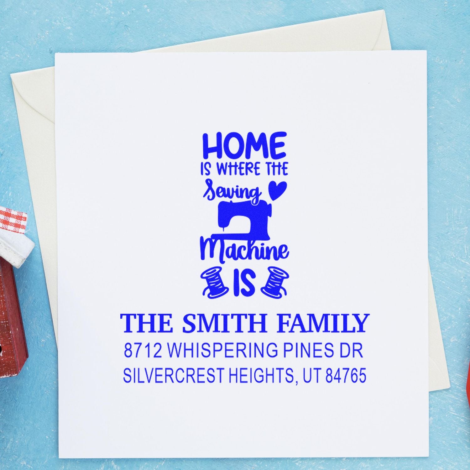 Custom address stamp with a home sewing machine design on white card, displayed with envelopes on a blue background.