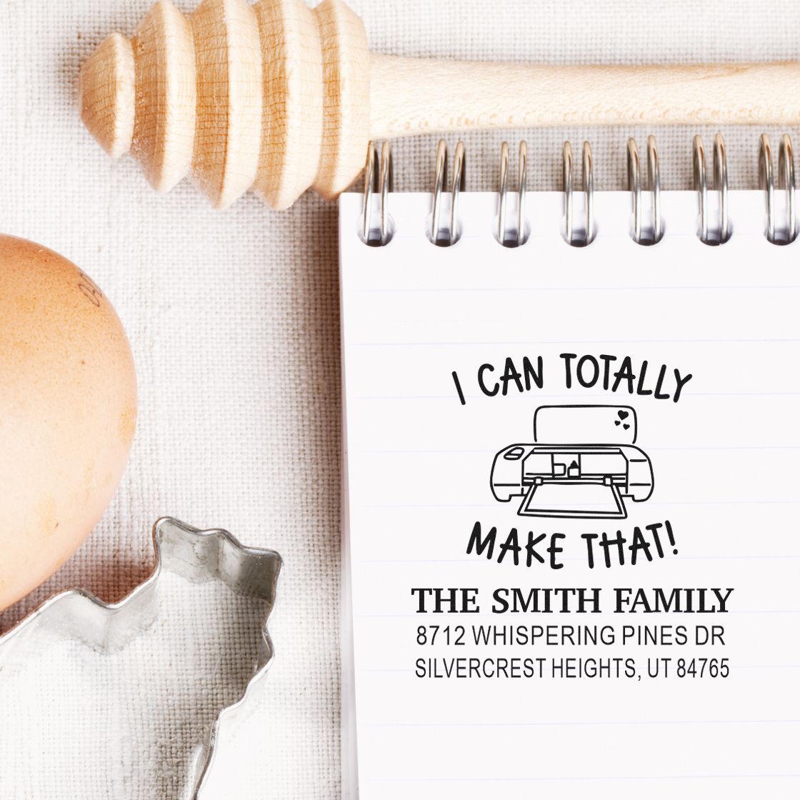 Custom return address stamp on notebook beside wooden stamp handle, with "I CAN TOTALLY MAKE THAT!" printer design and The Smith Family address.