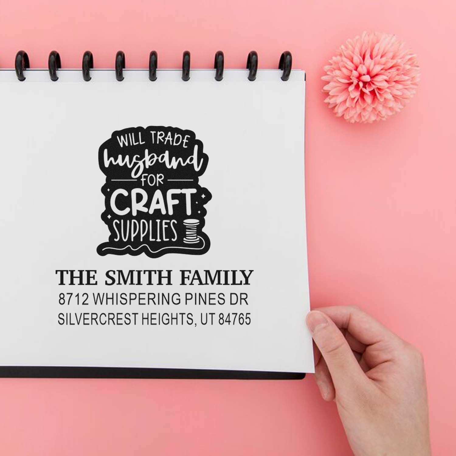 Custom address stamp on notebook page reading Will Trade Husband for Craft Supplies, held by hand on a pink background.