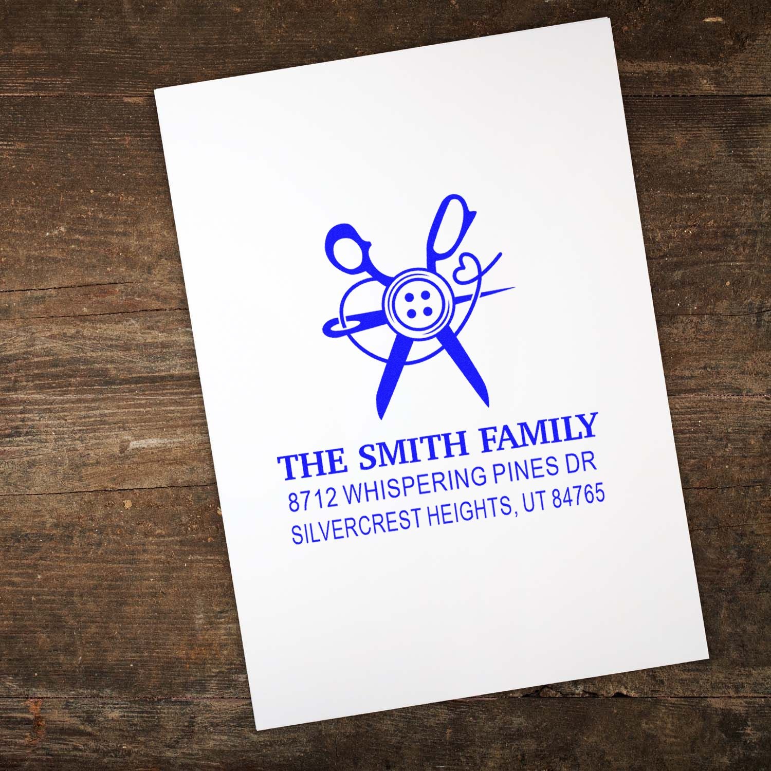 Custom family address stamp with blue scissors-and-button design on white paper, featuring The Smith Family address on a rustic wooden background.