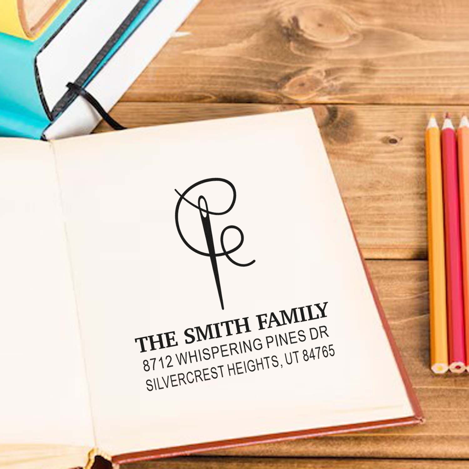 Custom return address stamp with monogram and The Smith Family on open notebook, styled on a wooden desk with colored pencils and notebooks.
