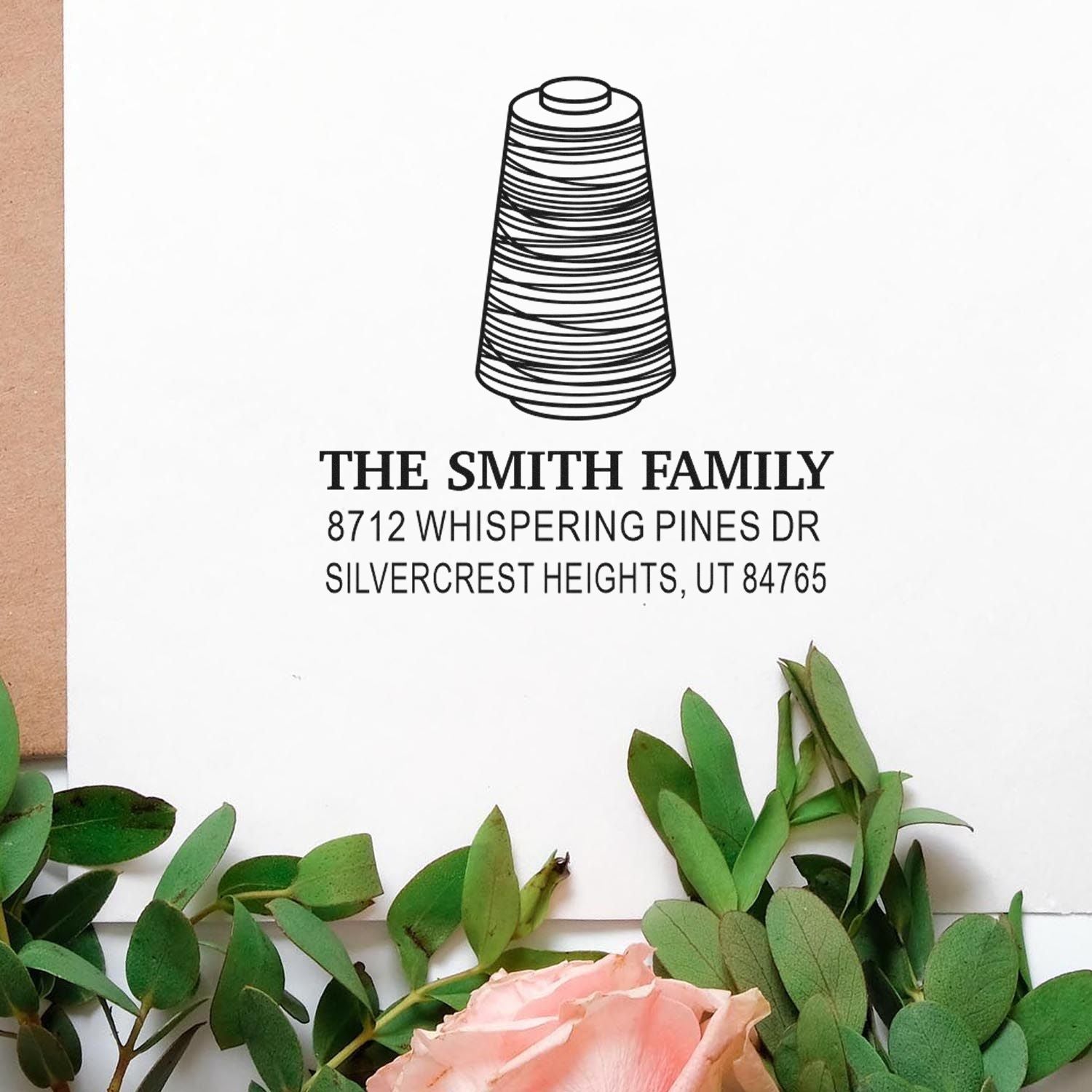 Custom address stamp with thread spool icon, showing The Smith Family and Silvercrest Heights, UT address on white paper, framed by greenery and a pink rose.