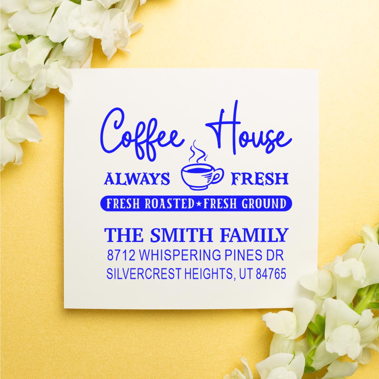 Custom coffee house address stamp with blue lettering, coffee cup icon, and Fresh Roasted Fresh Ground on a cream background with white flowers.