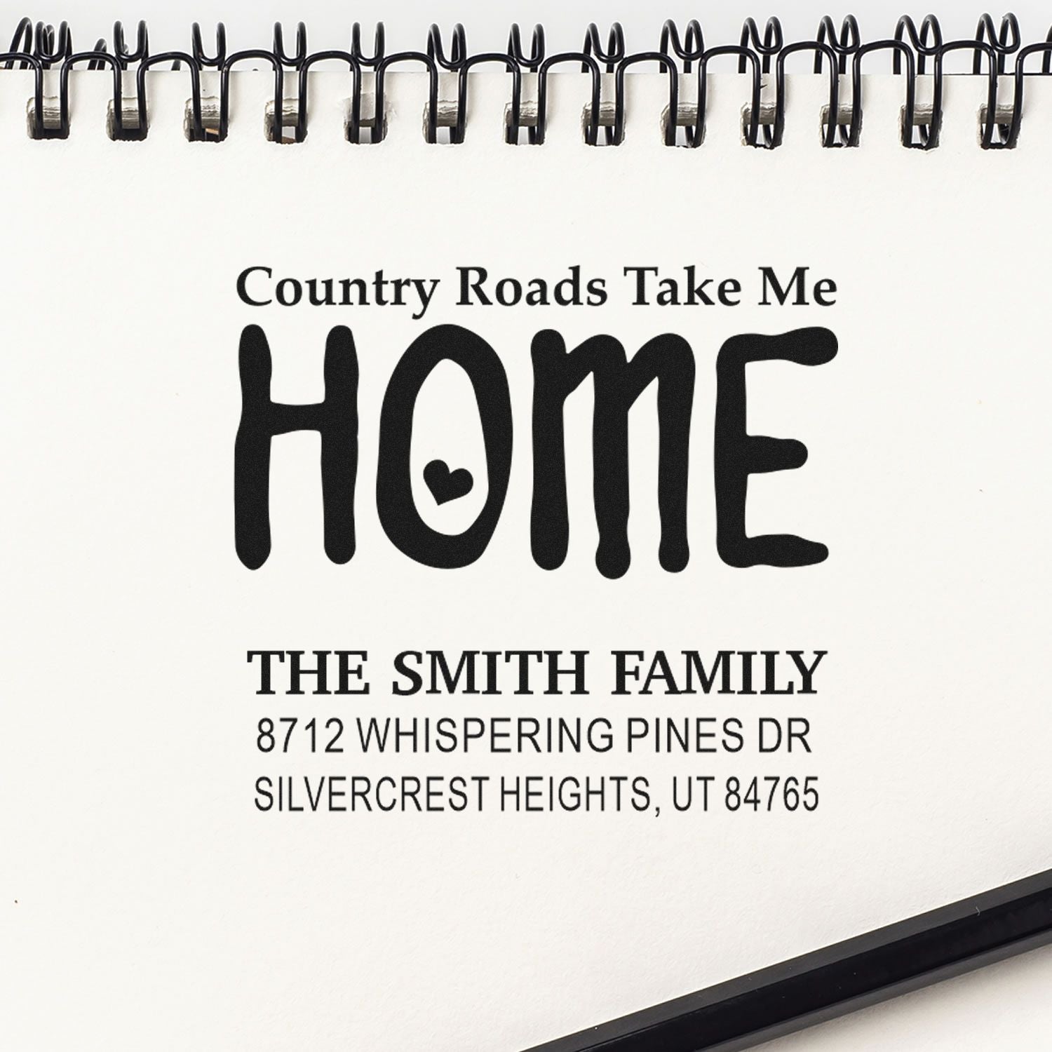 Custom home address stamp in a spiral-bound sample book, reading Country Roads Take Me Home with THE SMITH FAMILY and a Utah address.