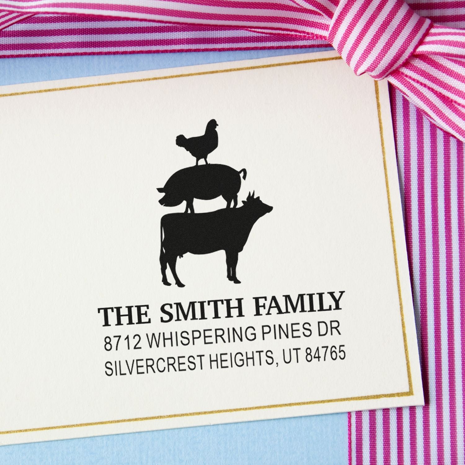 Custom family address stamp with chicken-on-pig silhouette on cream card, gold border, and pink striped ribbon.