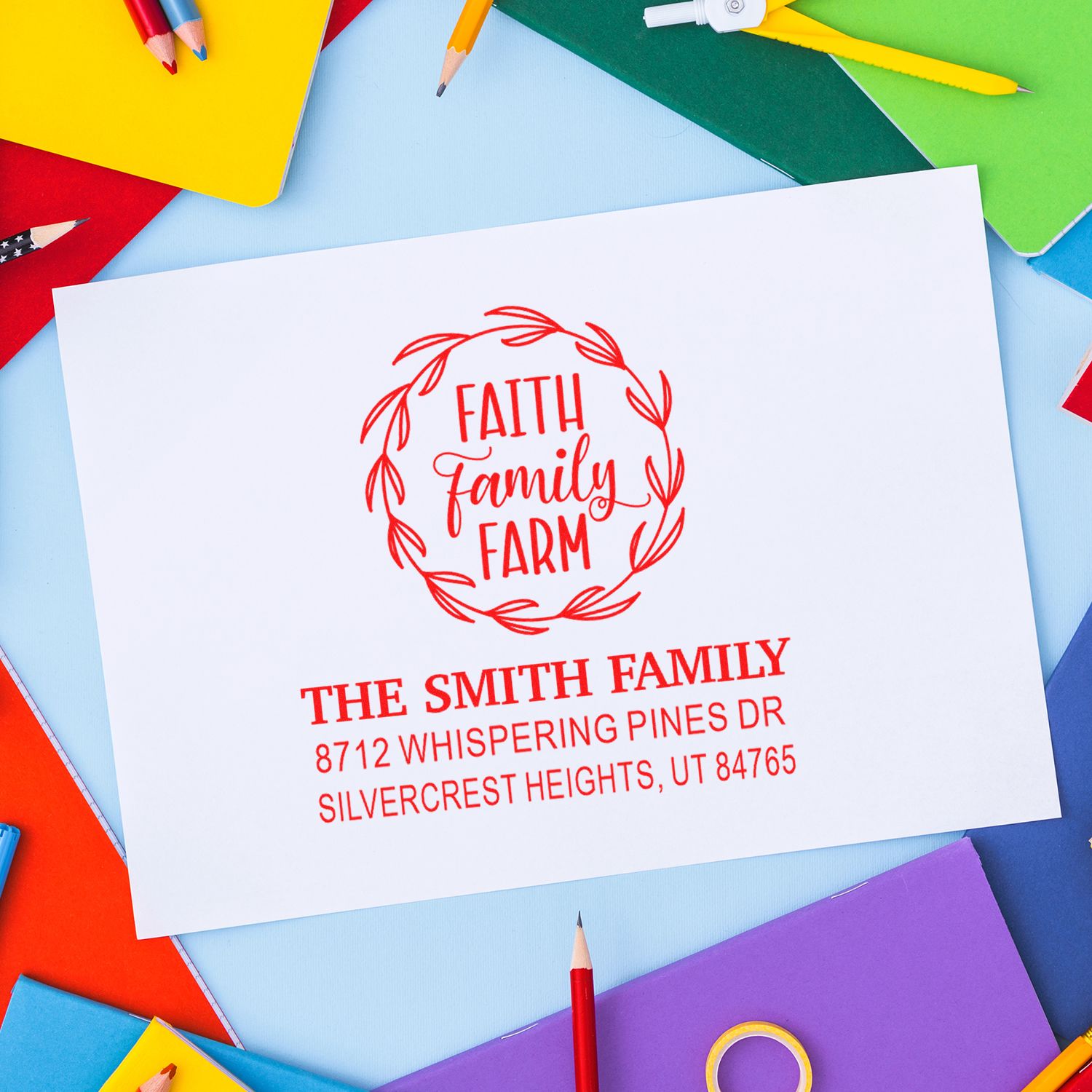 Custom self-inking stamp with Faith Family Farm logo and Smith family address, displayed on white paper with colorful pencils and notebooks.