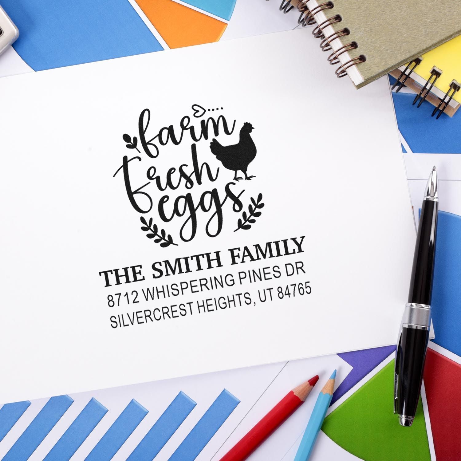 Custom farmhouse fresh eggs address stamp on white envelope, featuring chicken graphic and family name, surrounded by colorful stationery and pens.