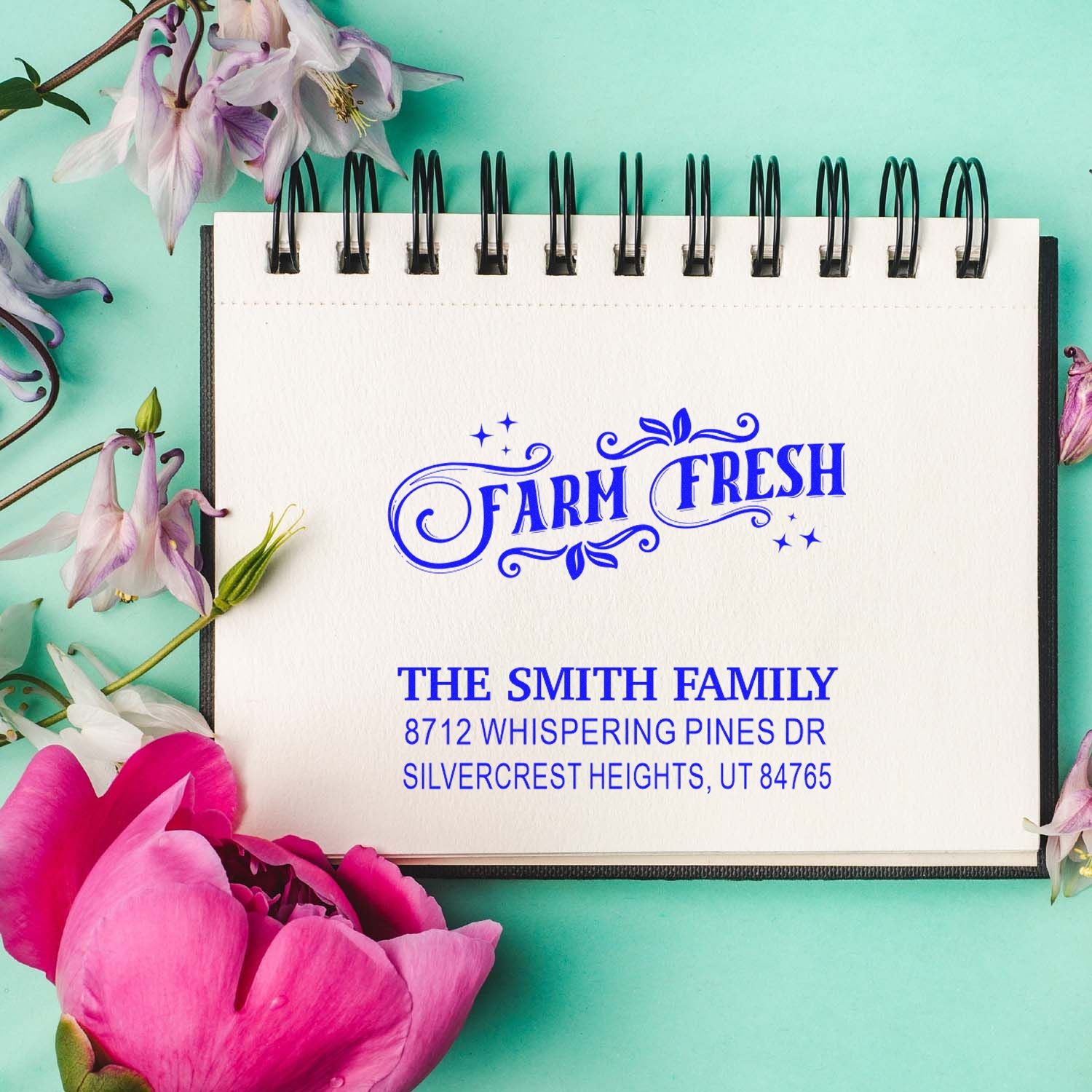 Custom Farm Fresh address stamp for The Smith Family on a spiral notebook, surrounded by flowers on a mint green background.