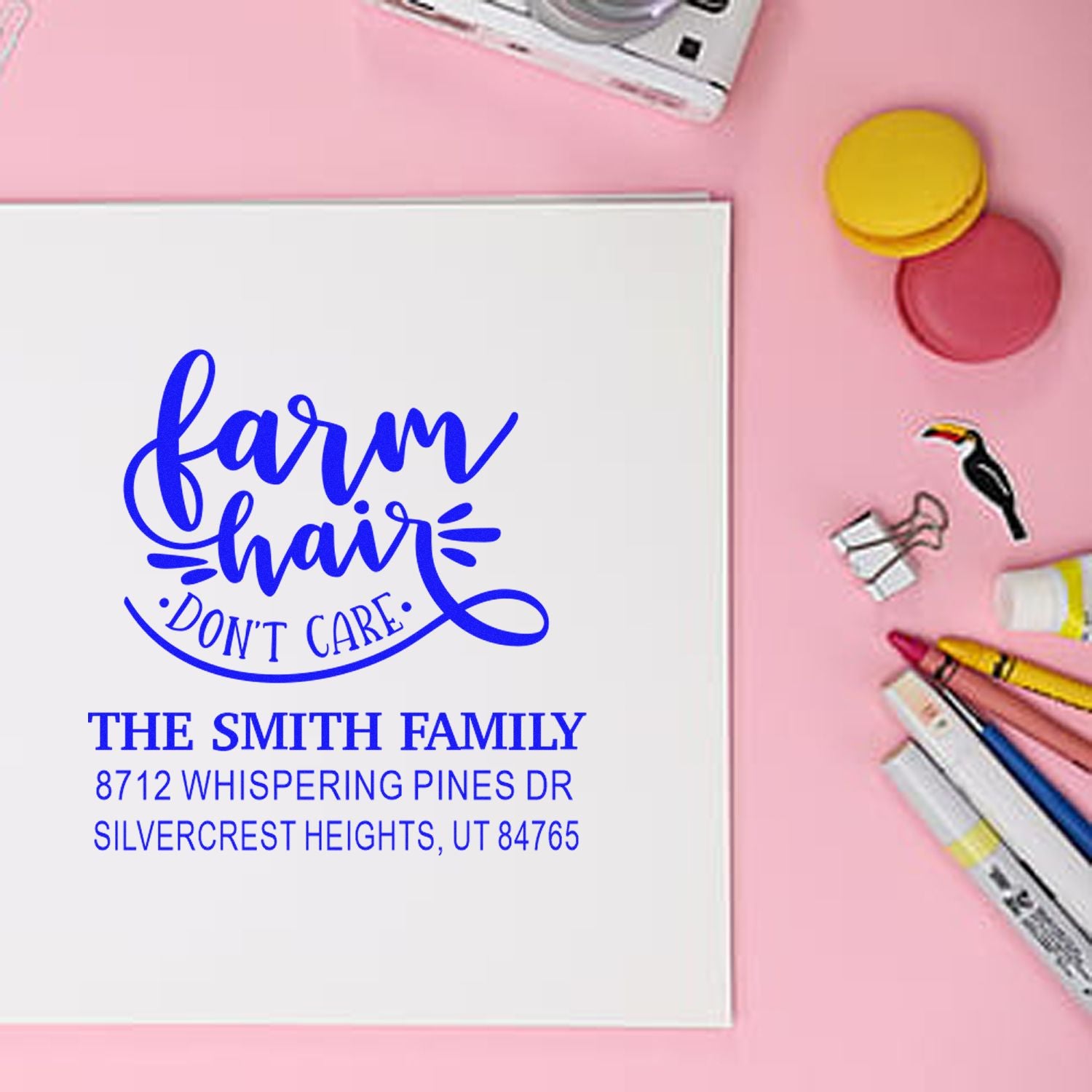 Custom farm hair dont care return address stamp on white card, set on a pink desk with pens, paper clips and ink pads.