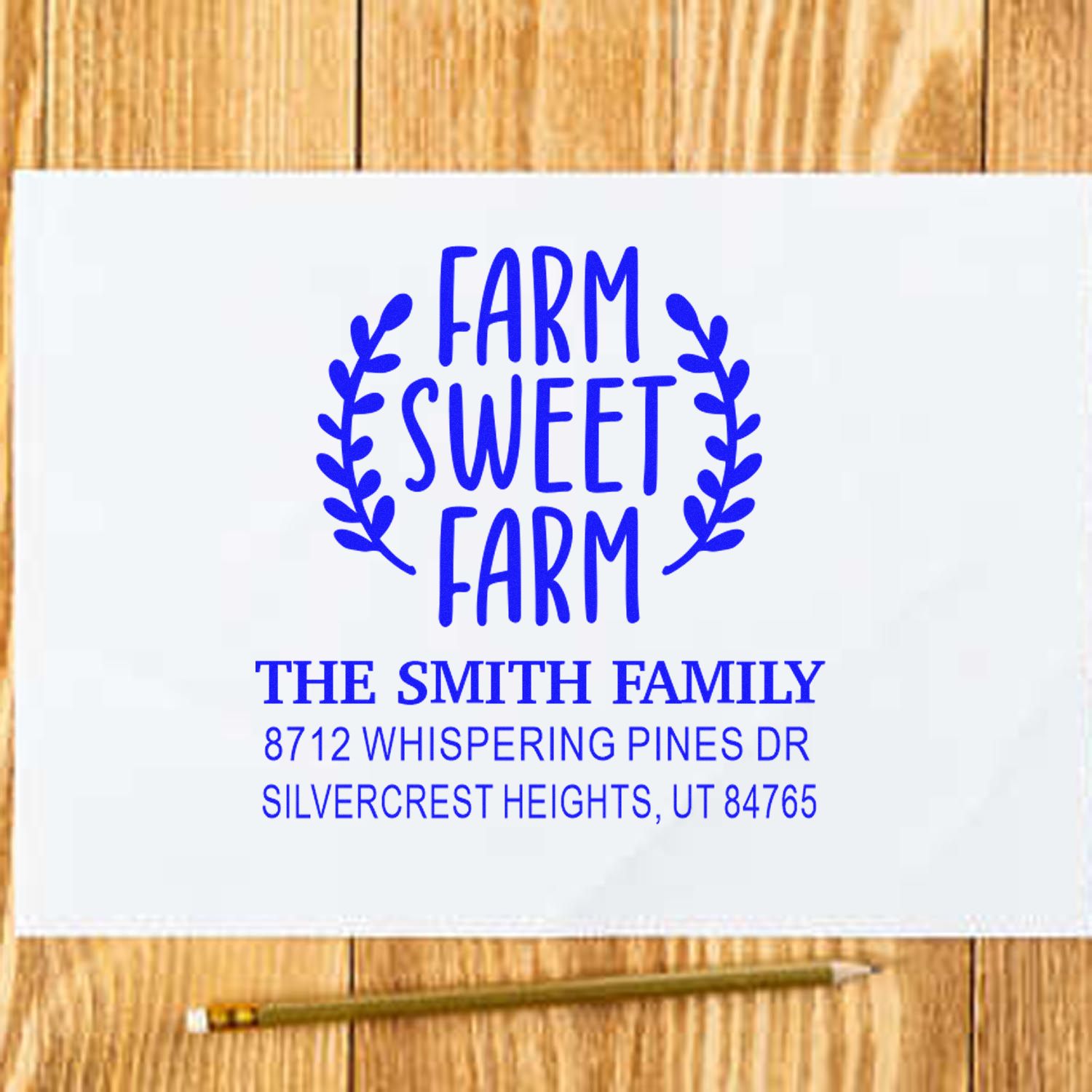 Custom Farm Sweet Farm address stamp in blue on white paper, shown on a wooden table with a pencil, featuring family name and mailing address.