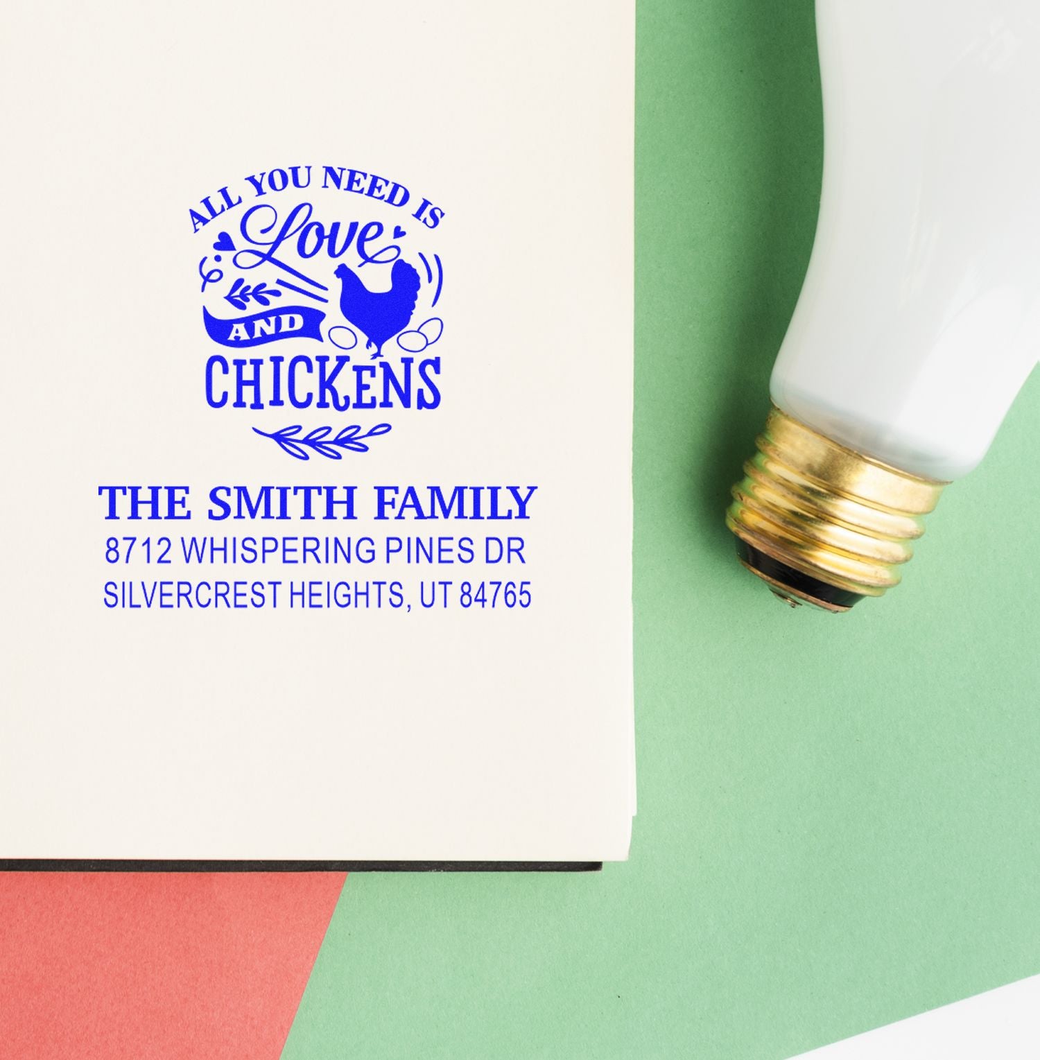 Custom chicken-themed address stamp in blue ink on paper, reading All You Need Is Love and Chickens, beside a self-inking stamp handle.