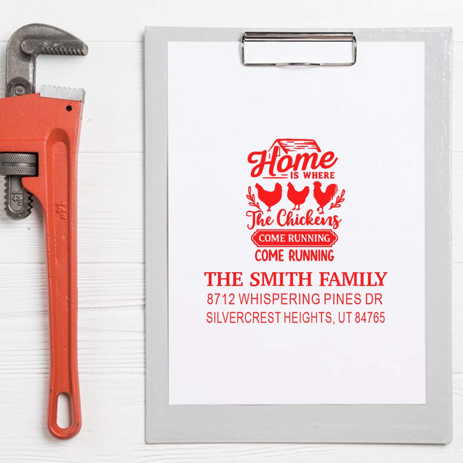 Custom farmhouse address rubber stamp on clipboard, red chicken design with family name and address beside a pipe wrench.